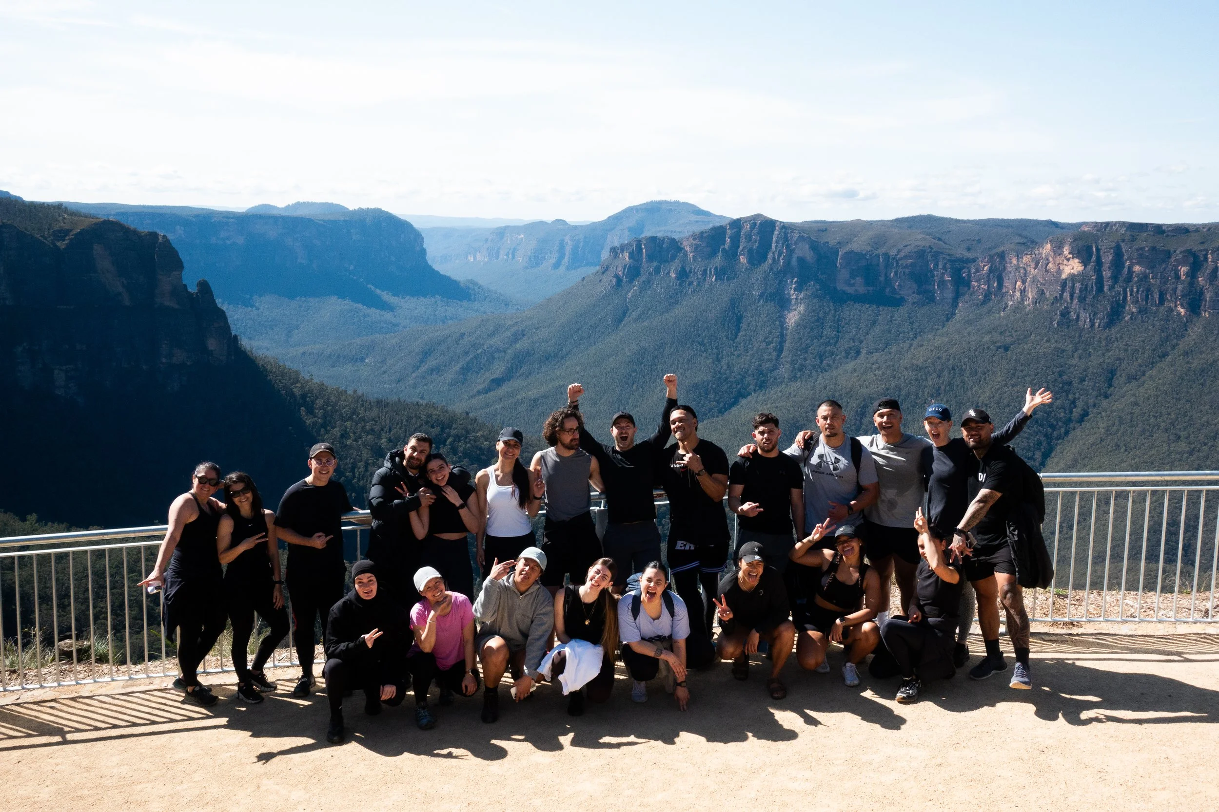 Group of people taking a photo on a wooden platform with a mountain and valley landscape in the background.