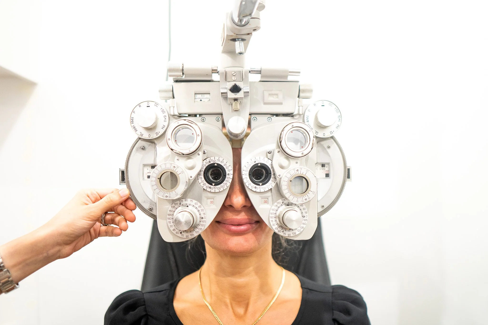 A woman sitting in an eye examination chair with a phoropter over her eyes, used for eye testing and vision correction.