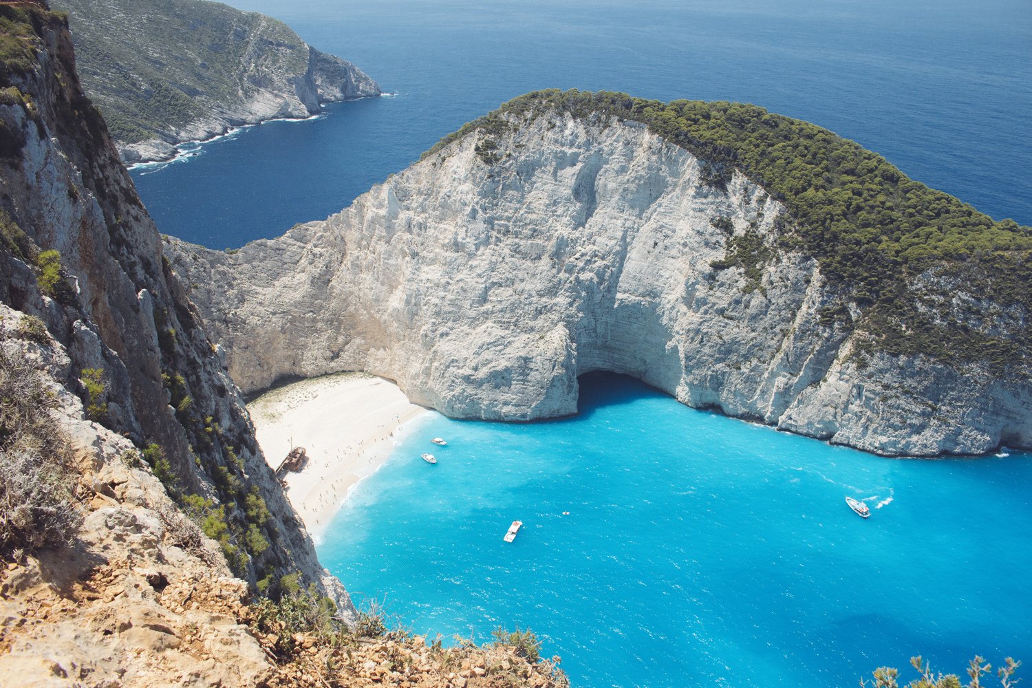 View of Navagio Beach, also known as Shipwreck Beach, on the island of Zakynthos, Greece, with a notable large sea cave, white sandy beach, and turquoise waters surrounded by steep cliffs covered with greenery.