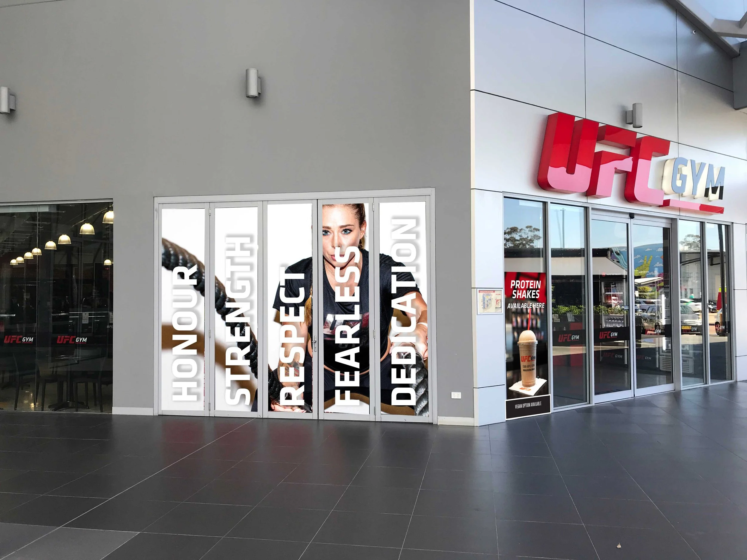 UFC GYM storefront with motivational banners and a sign advertising protein shakes outside
