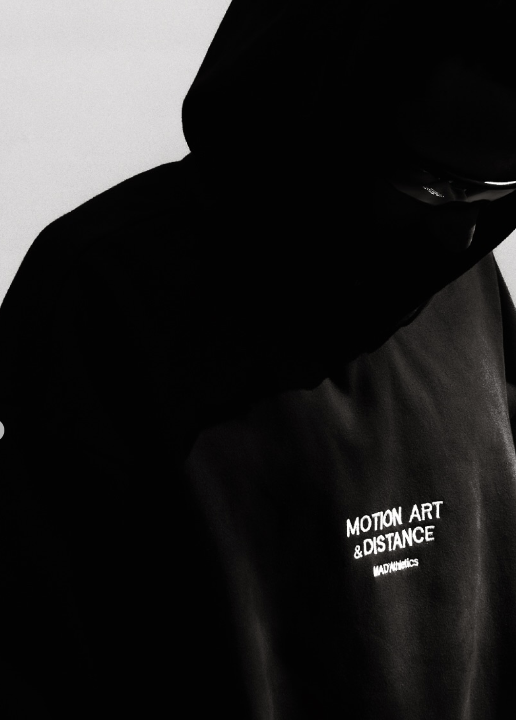 A person wearing black clothing and sunglasses with text on the shirt reading 'Motion Art & Distance MAD ATHLETICS'.