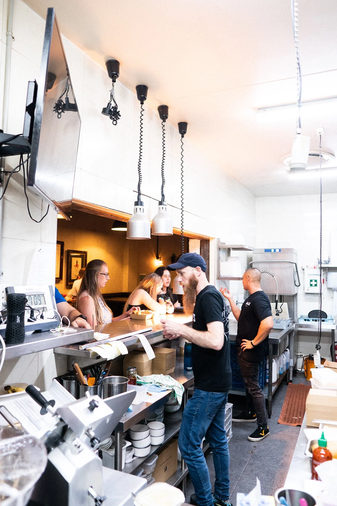 A busy restaurant kitchen with staff preparing food and customers waiting at the counter.