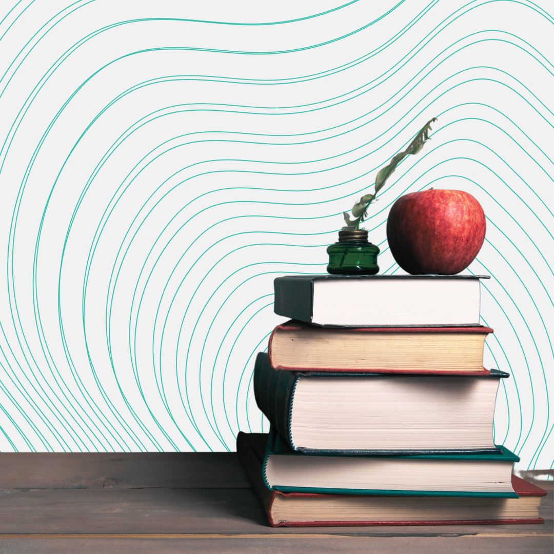 Stack of six closed books on a wooden surface, with an apple and an inkwell with a feather quill on top, against a white wall with light blue contour line patterns.