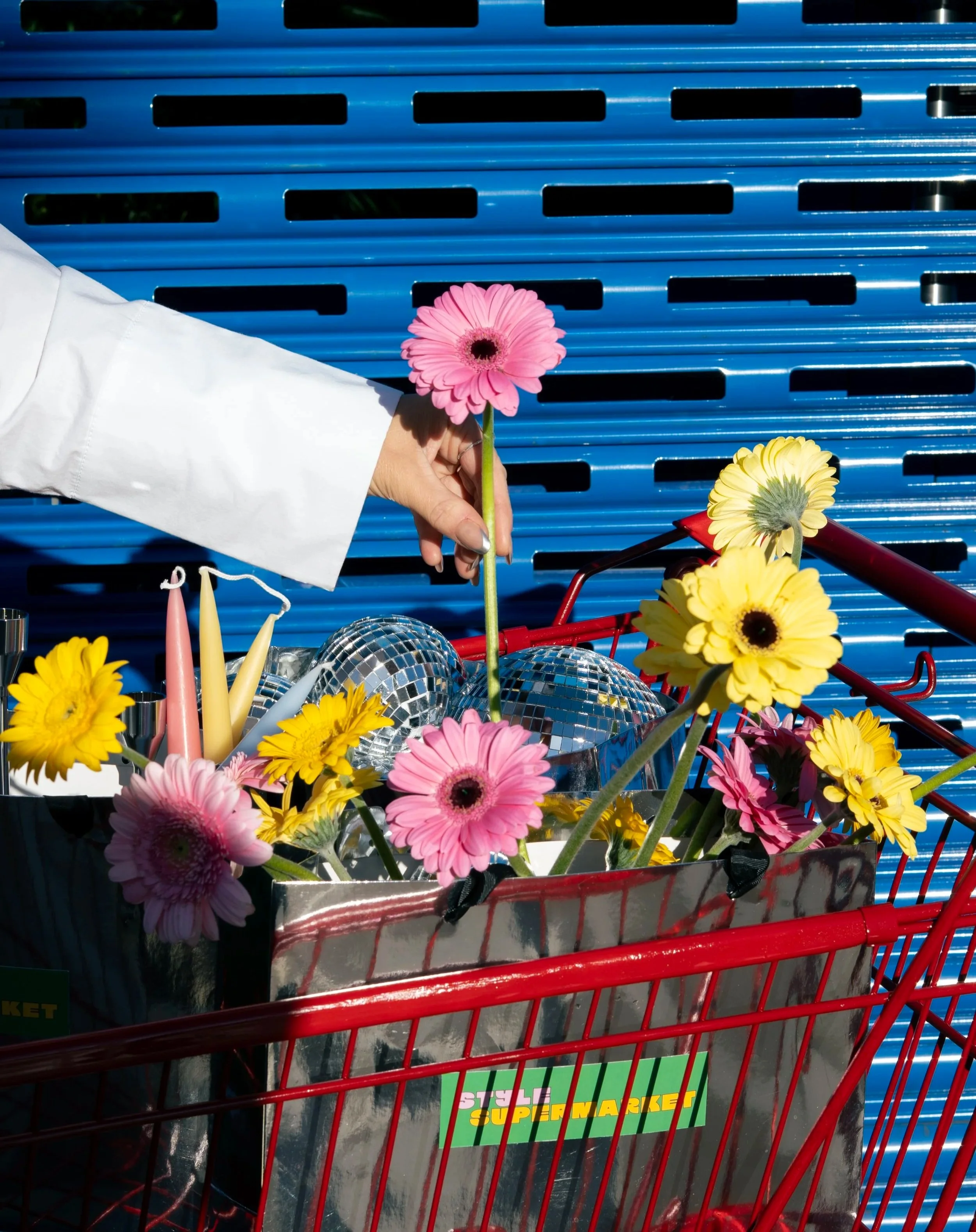 red trolley filled with styling items, like flowers, branded silver bags and canles and disco balls on a blue shutter door background