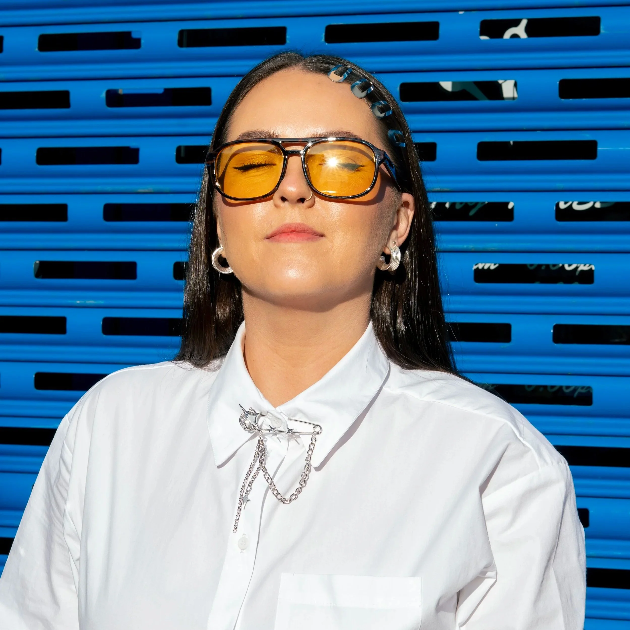 abie the stylist with orange glasses on and a white shirt against a blue shutter door background