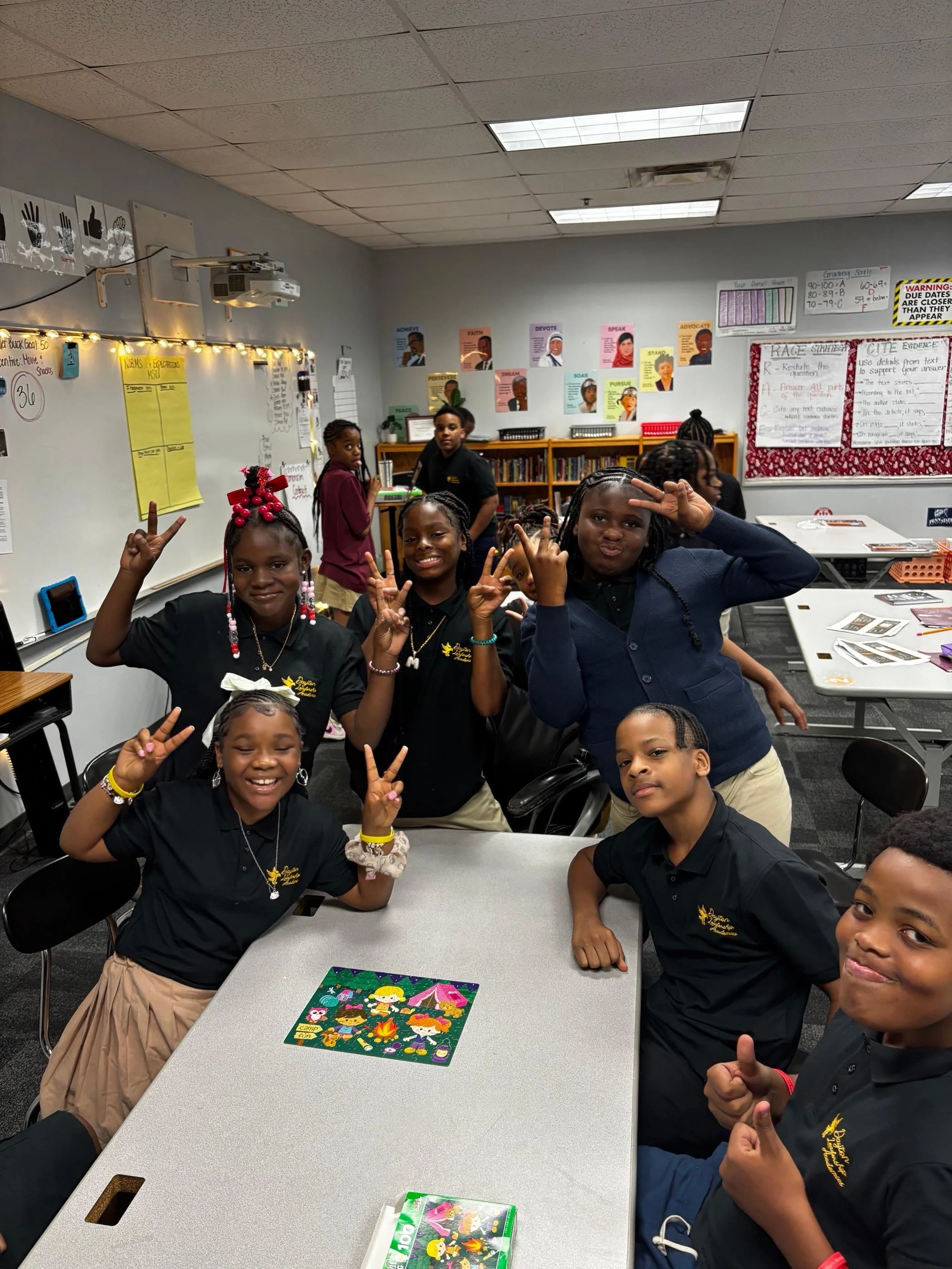 A group of children in a classroom making peace signs and smiling at the camera.