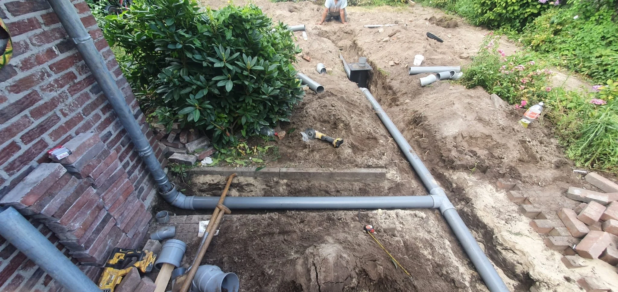 Rioolaanleg in de tuin: nieuwe afvoerleiding in de gegraven sleuf langs de gevel