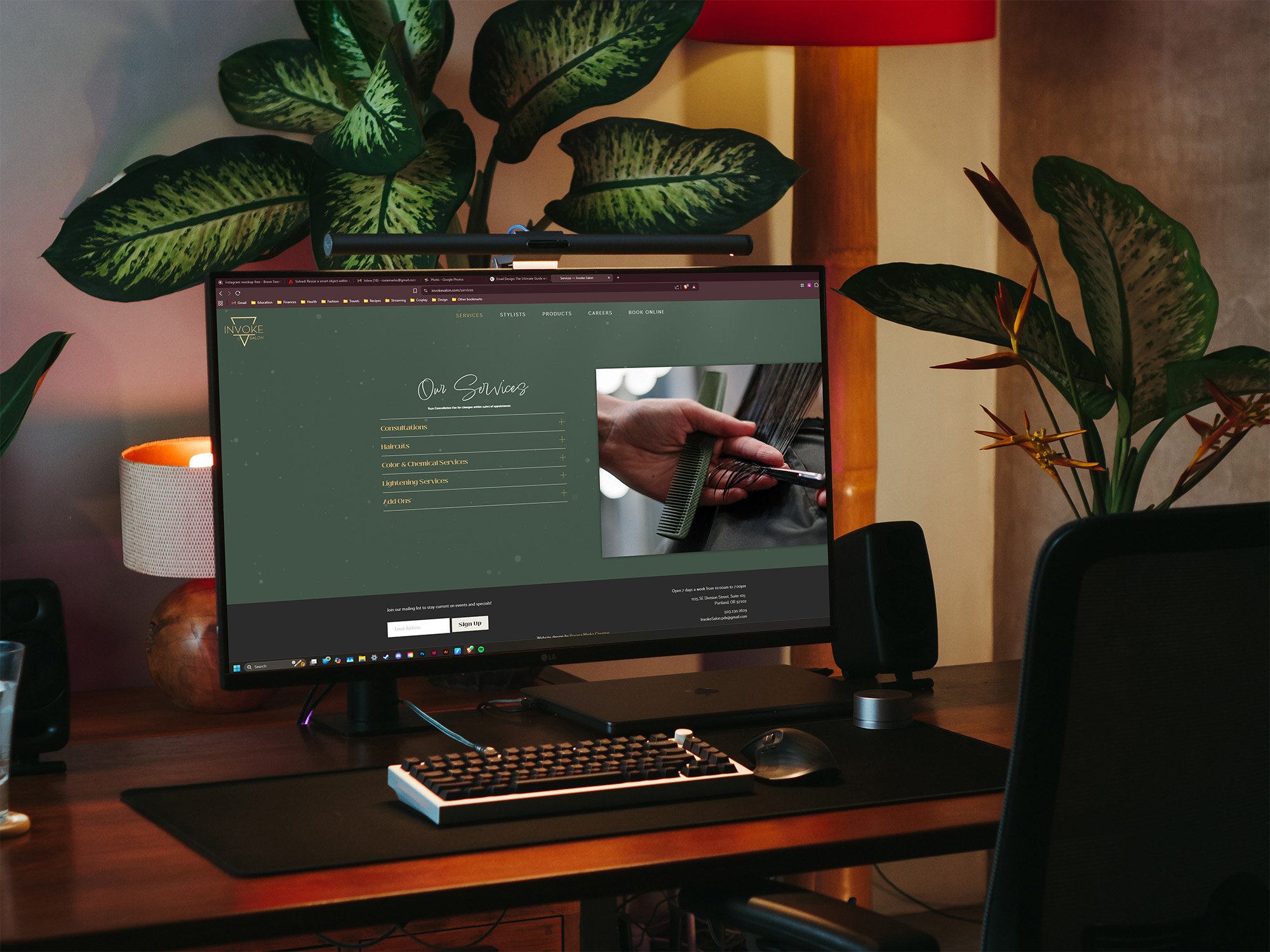 Modern workspace with a desktop computer displaying a barbershop website’s “Our Services” page. Desk includes keyboard, mouse, red-shaded lamp, plants, candle, and glass of water for a cozy vibe.