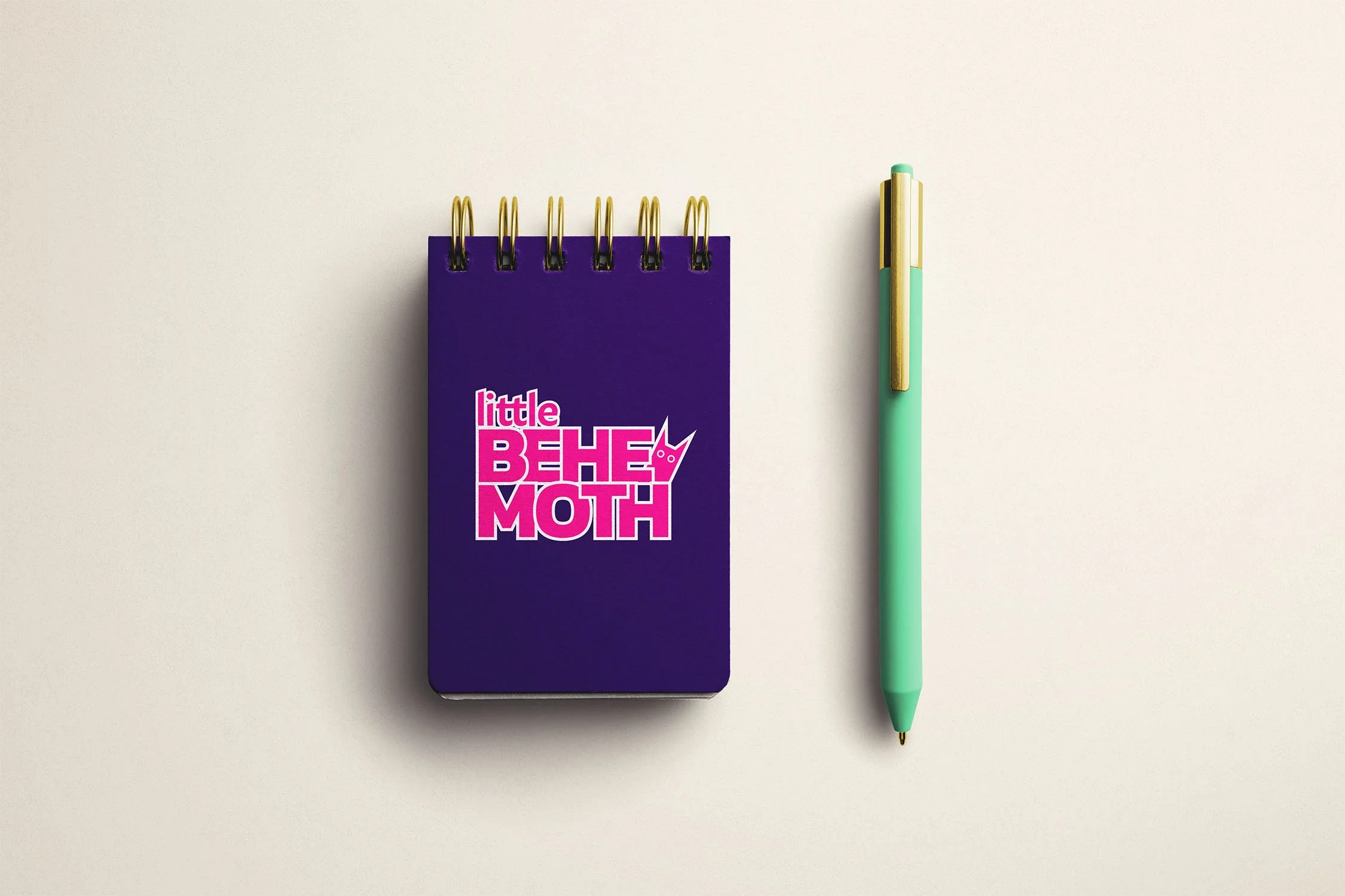 Mockup of a notepad and pen with Little Behemoth's purple, turquoise, and neon pink color palette.