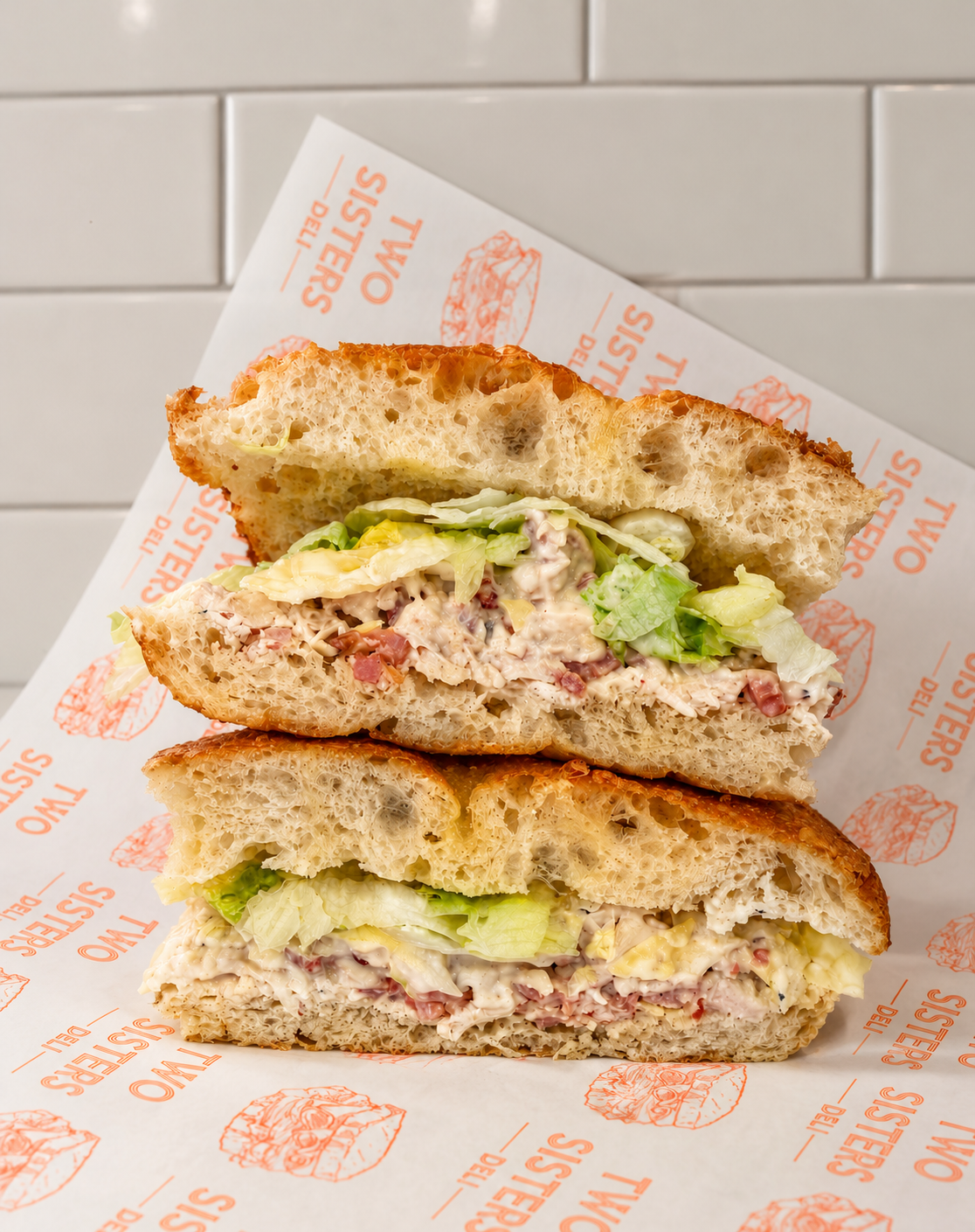 Close-up of a shredded beef sandwich with barbecue sauce on a sandwich bun, placed on branded paper with Toledo Streakers logo, against a gray tiled background.