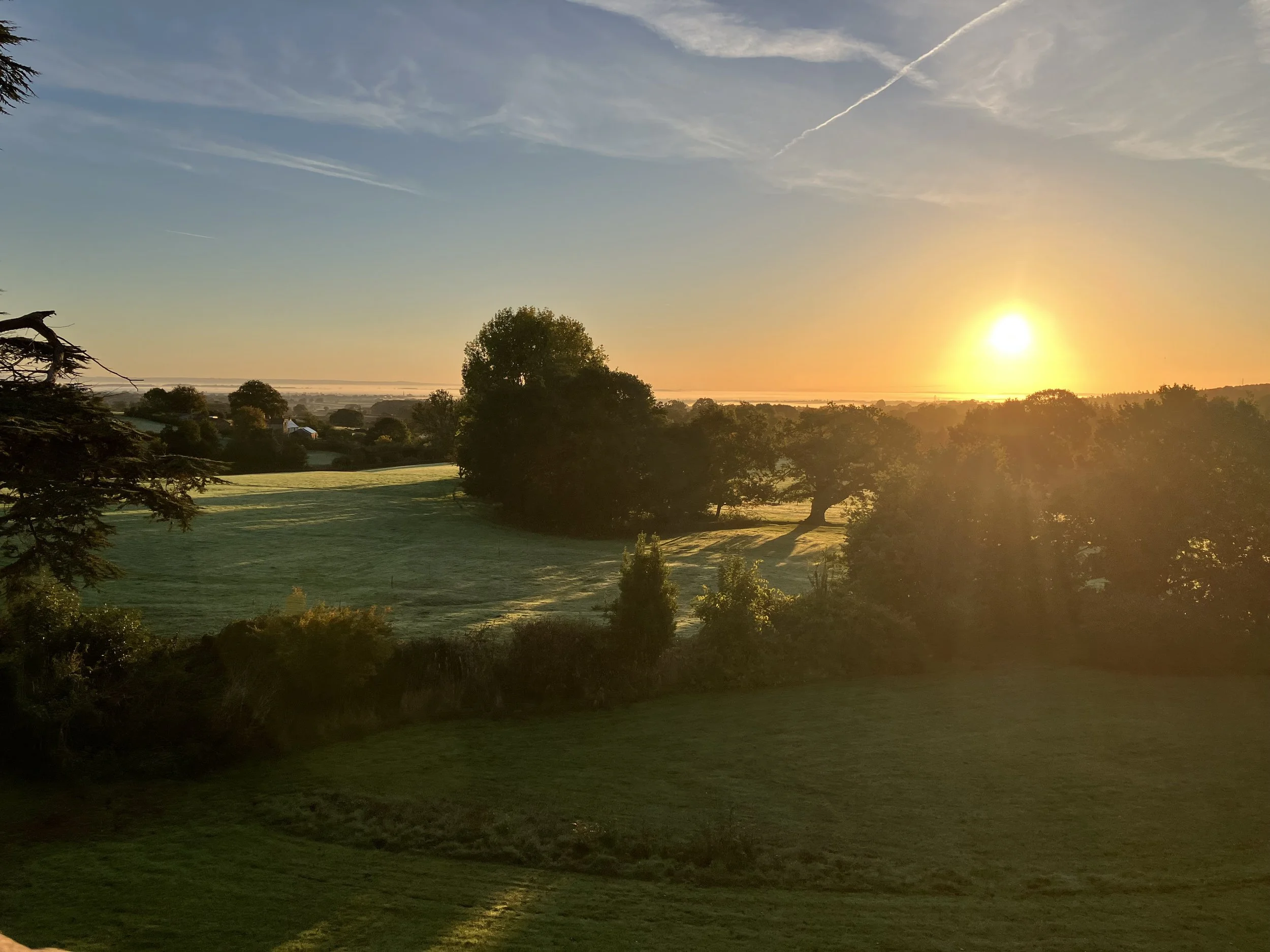 Sunset over a green landscape with trees and rolling hills.