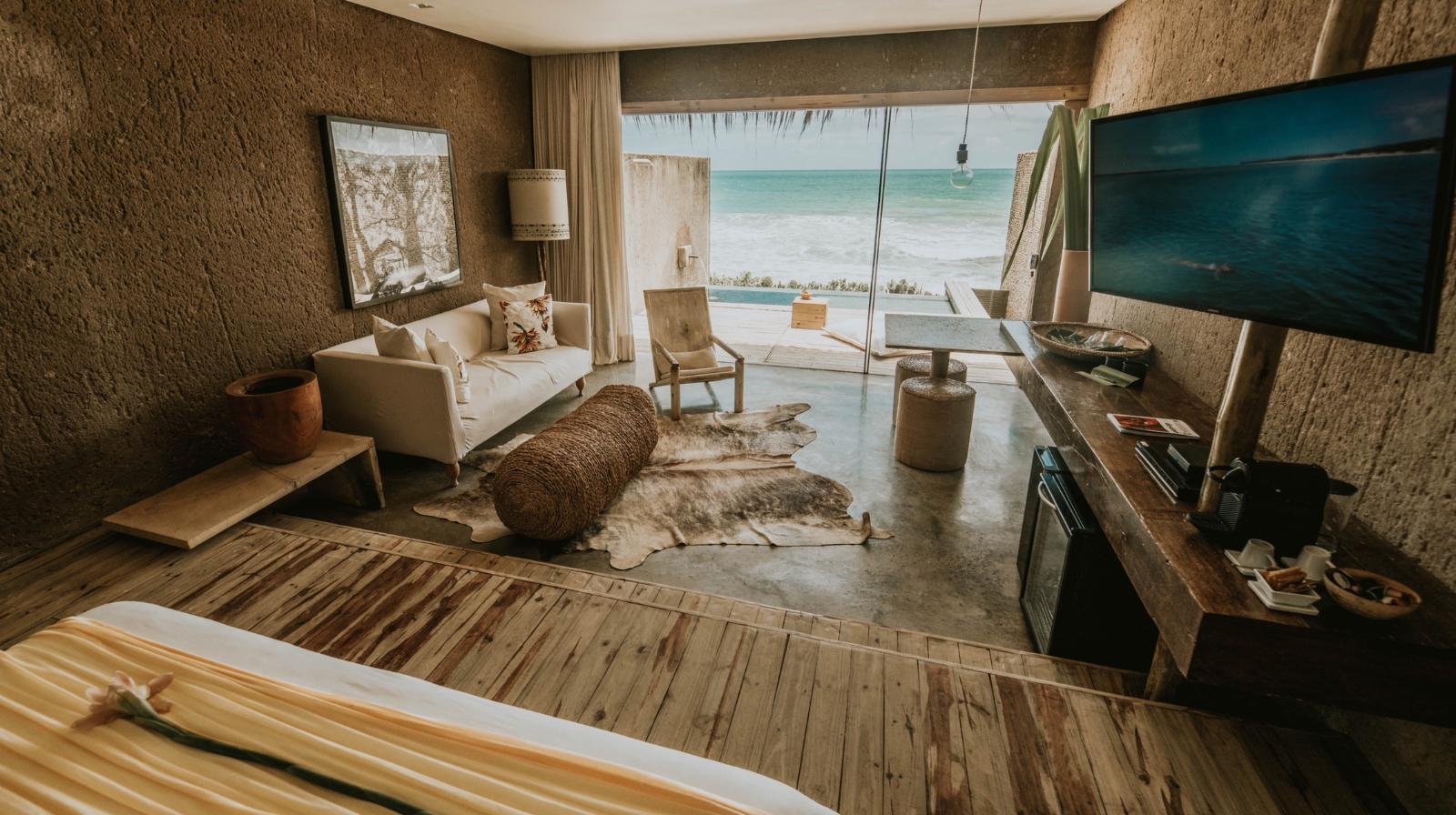 Oceanfront suite at Kenoa Resort in Barra de São Miguel, Brazil, with natural textured walls, modern rustic decor, and panoramic views of the Atlantic Ocean from a private terrace.