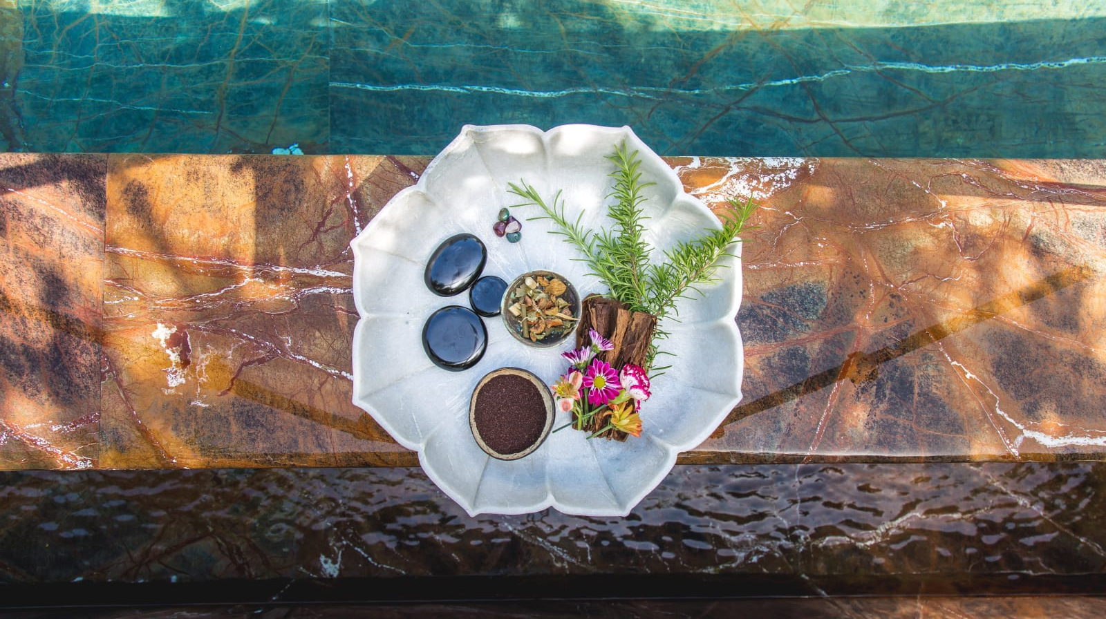 Overhead view of spa treatment tray with natural botanicals and essential oils over marble soaking tub