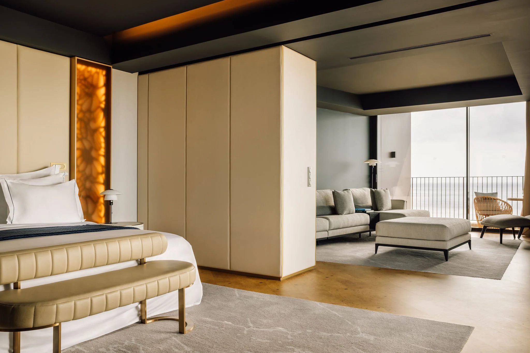 Spacious hotel suite with contemporary design, neutral palette, custom furniture, and floor-to-ceiling windows overlooking the ocean—clean lines and understated luxury.