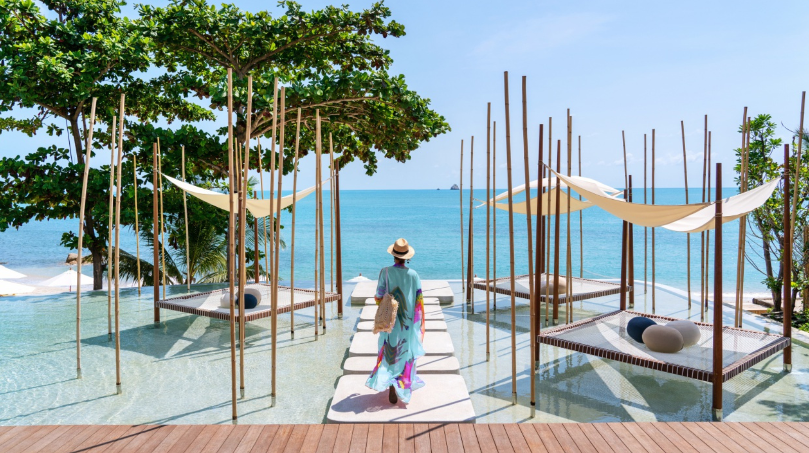 Guest walking along modern wooden walkway over water at Six Senses Samui with Gulf of Thailand views