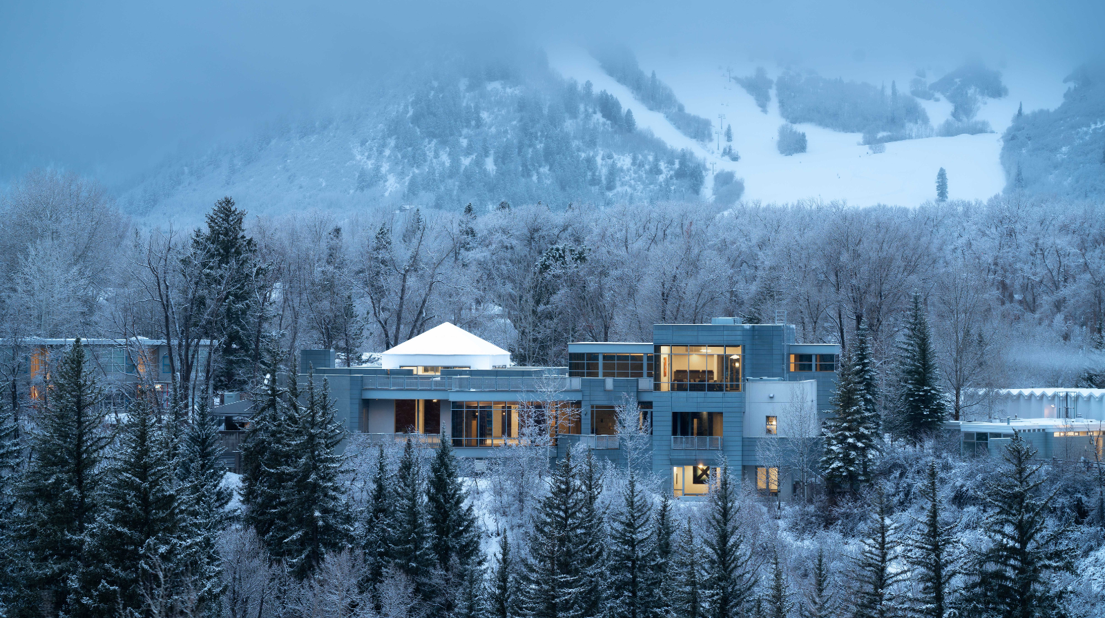 Aspen Meadows Resort modern luxury hotel covered in snow with mountain ski slopes in background Colorado