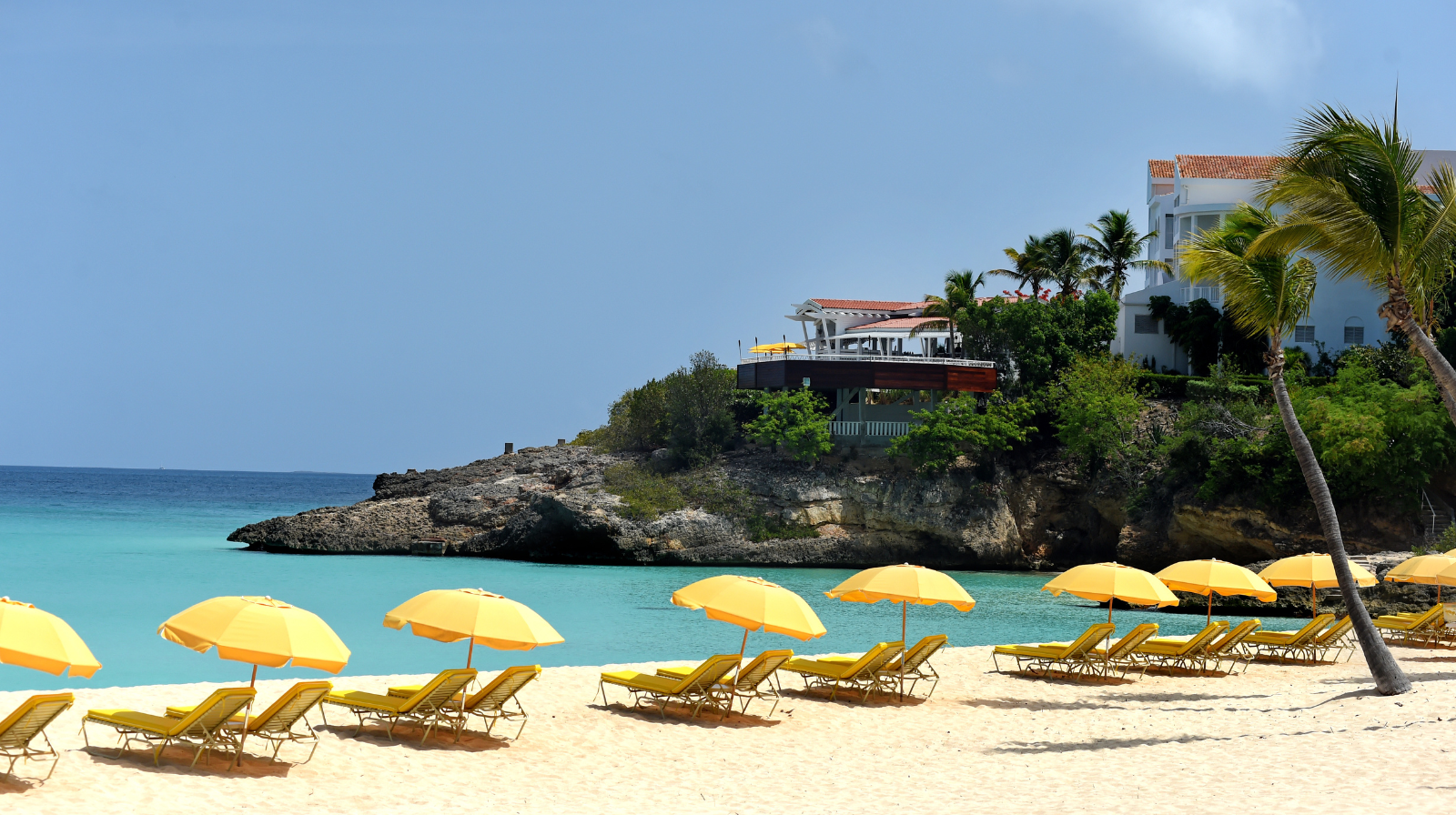 Beachfront at Malliouhana Resort in Anguilla with rows of yellow umbrellas and lounge chairs on pristine white sand, overlooking clear Caribbean Sea.