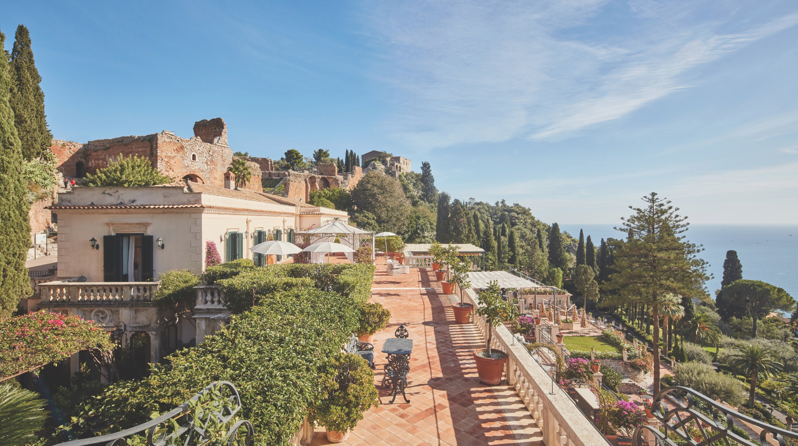 Grand Hotel Timeo, A Belmond Hotel in Taormina, Sicily, Italy, featuring a sunlit terrace, Mediterranean gardens, and views of ancient ruins and the Ionian Sea.