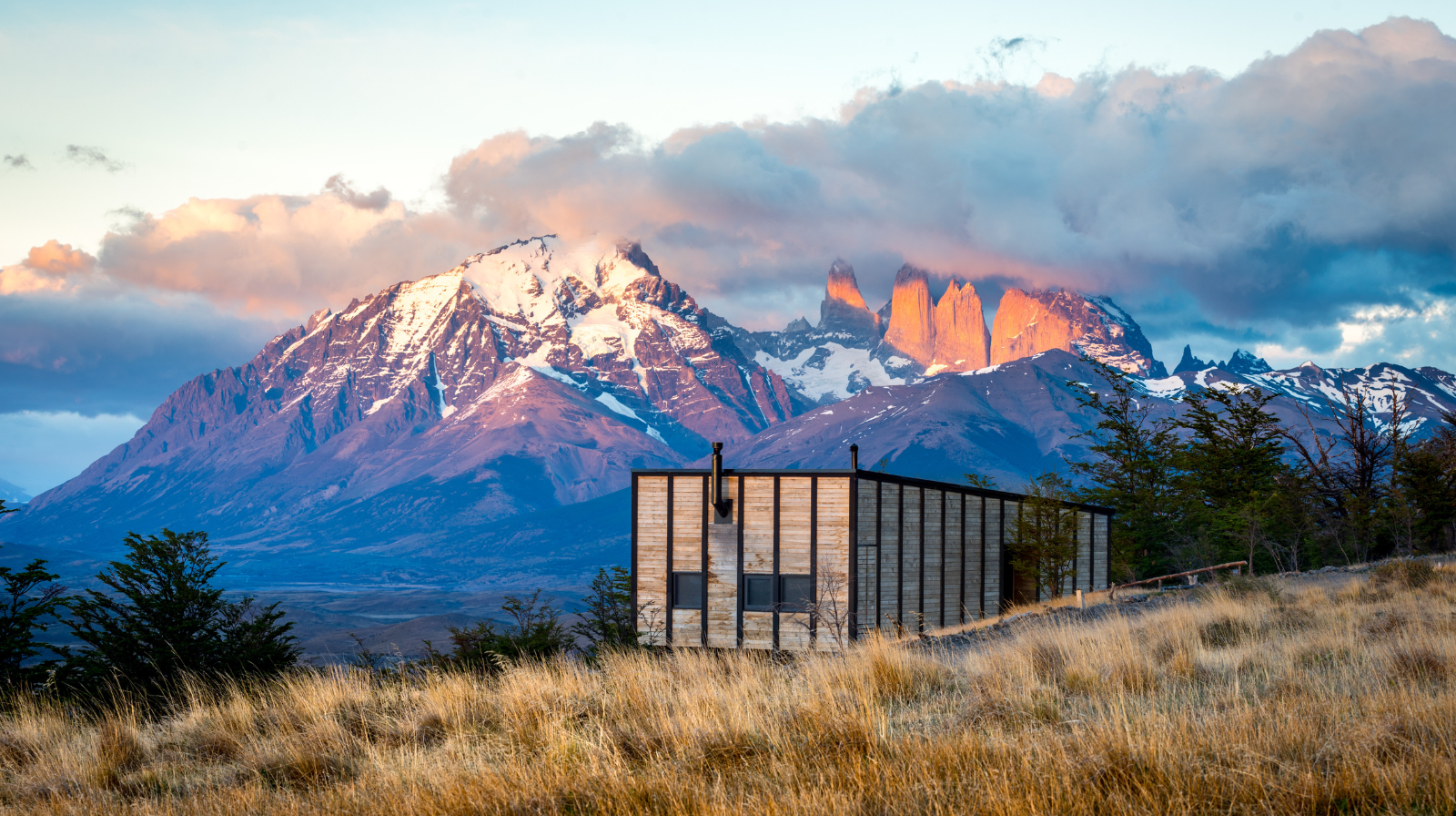 Modern luxury lodge with floor-to-ceiling windows overlooking Torres del Paine mountains at sunset in Patagonia, Chile