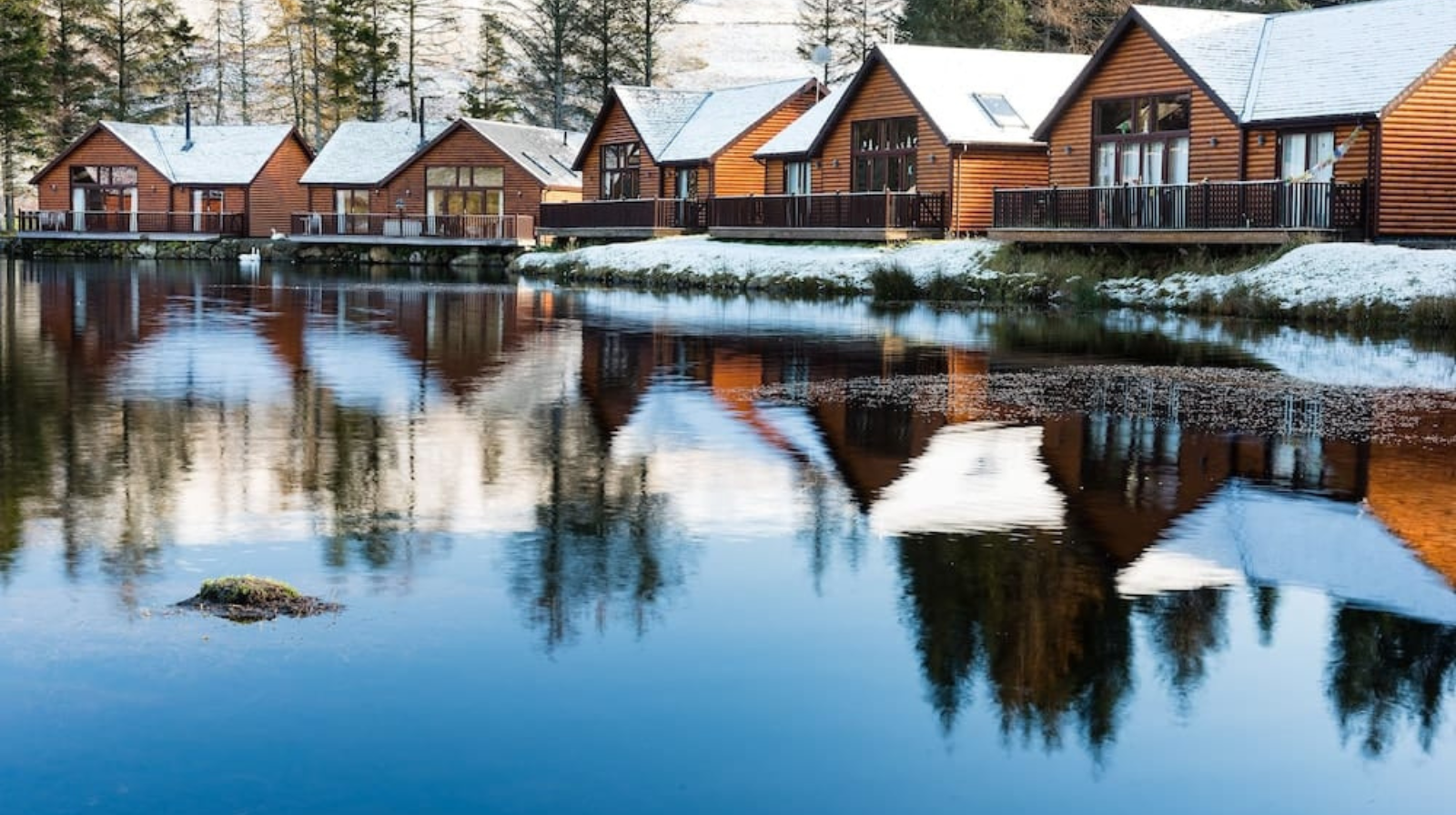Traditional wooden lodge cabins reflecting in still loch waters during winter in the Scottish Highlands