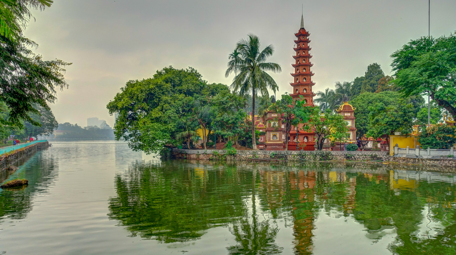 Red pagoda temple reflecting in calm river waters surrounded by tropical greenery in Hoi An's old town