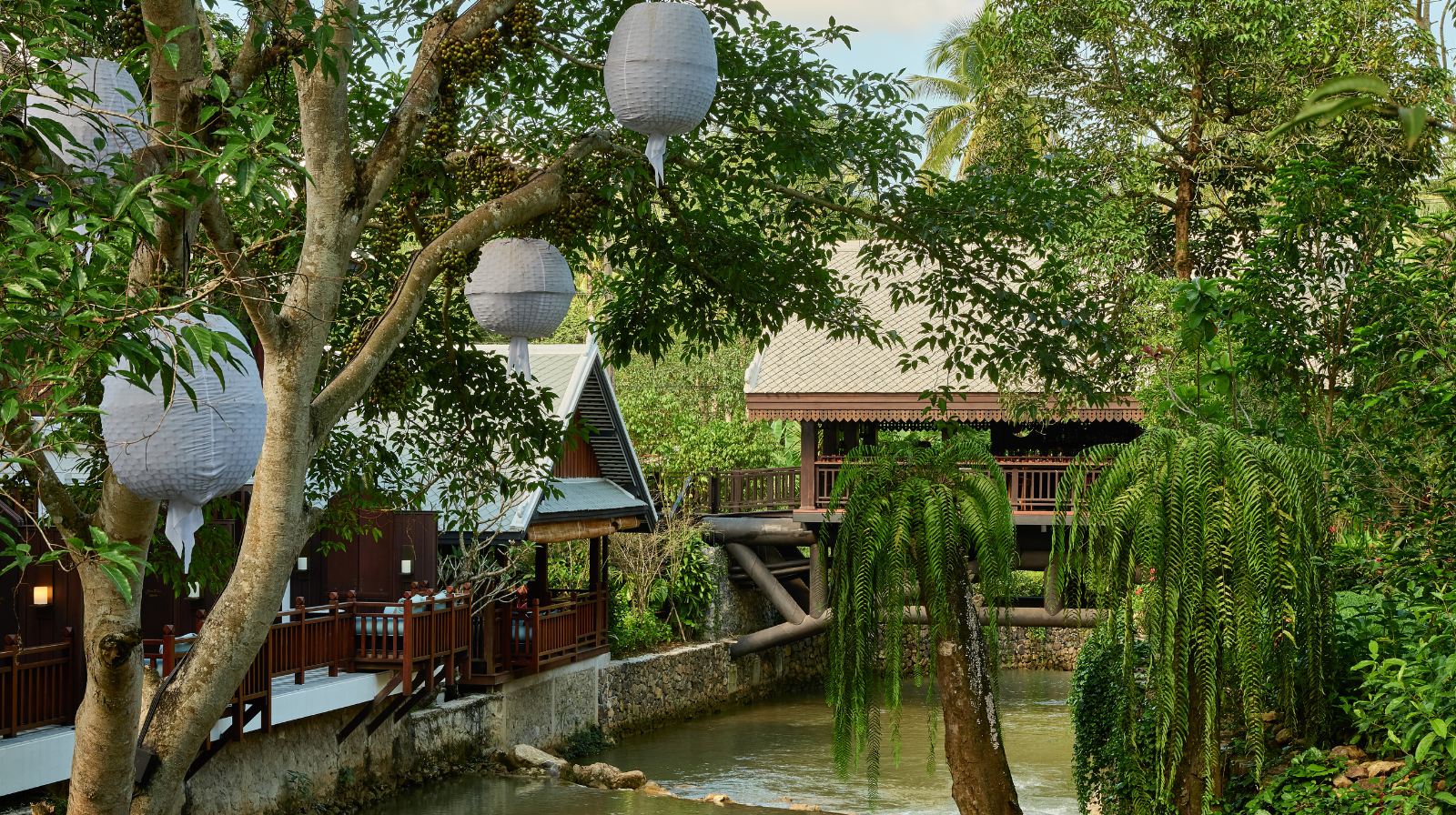 Traditional Lao wooden pavilions with paper lanterns over water at Rosewood Luang Prabang surrounded by jungle