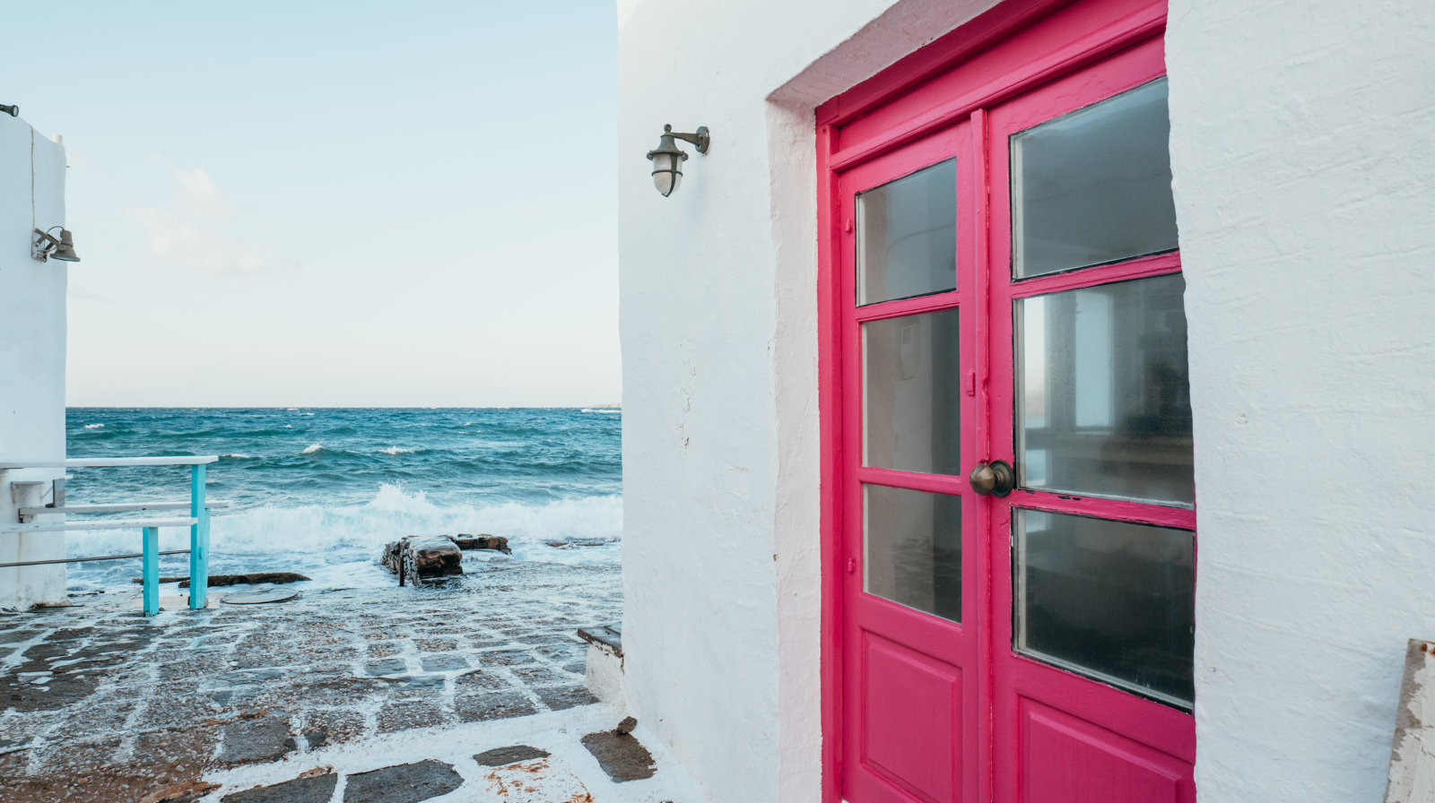 Bright pink door of whitewashed building overlooking turquoise Aegean Sea in Greek islands