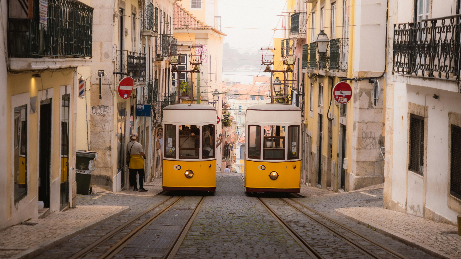 Traditional yellow trams on narrow cobblestone street in historic Alfama neighborhood, Lisbon