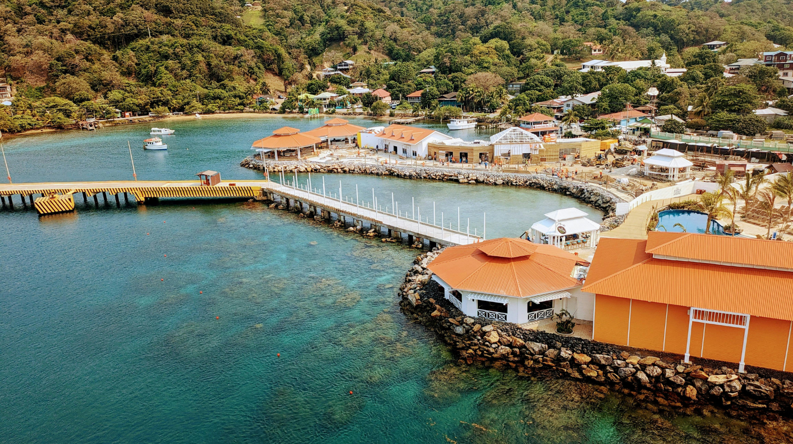 Ibagari Boutique Hotel in Roatán, Honduras, with orange rooftops, waterfront pier, turquoise Caribbean waters, and lush tropical landscape.