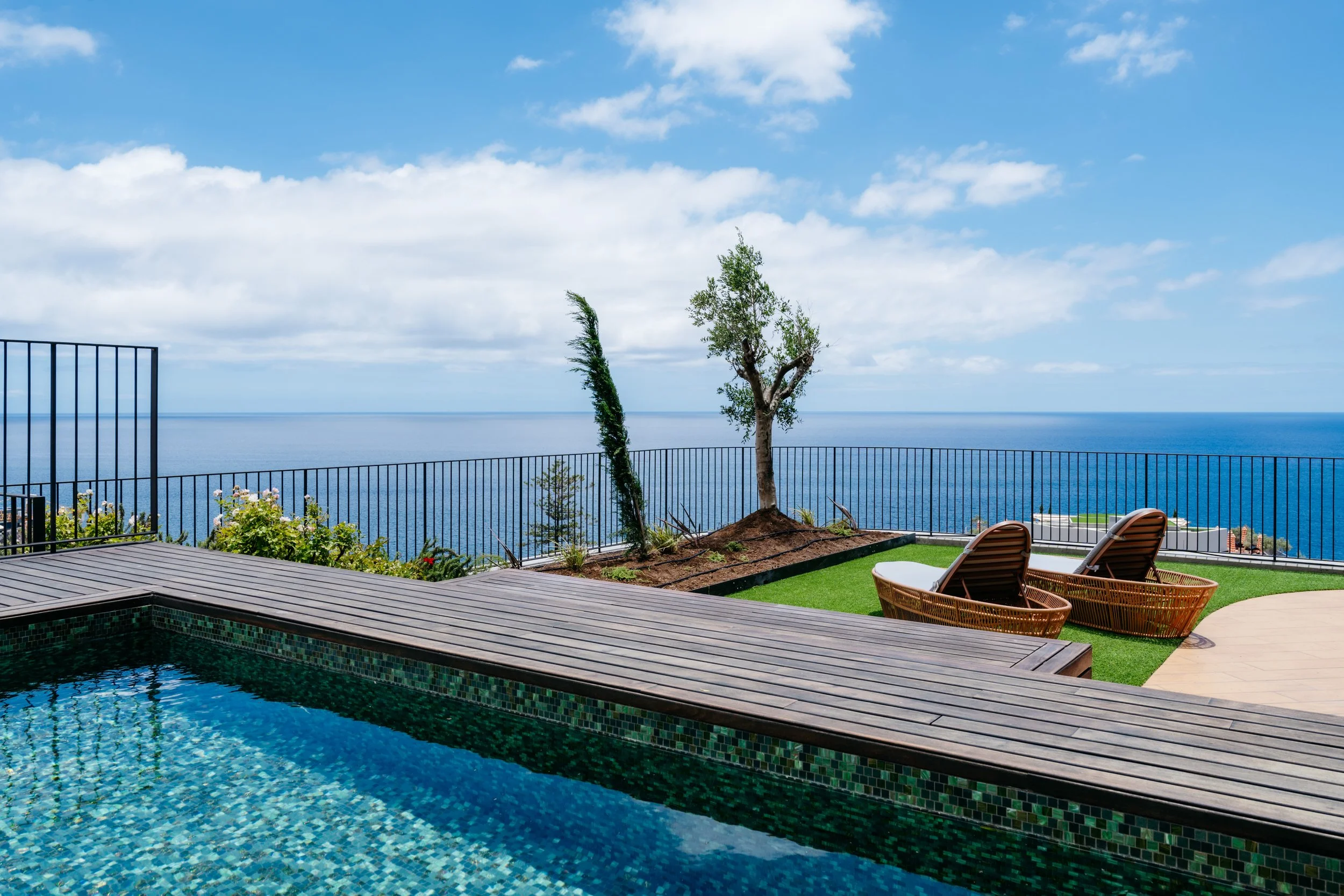 Private hotel pool and terrace with wicker loungers, minimalist landscaping, and panoramic Atlantic Ocean views in Funchal, Madeira—serene, modern, and uncluttered.