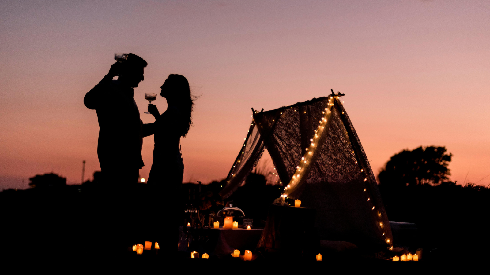 Couple toasting wine at sunset with candlelit glamping tent for romantic destination wedding