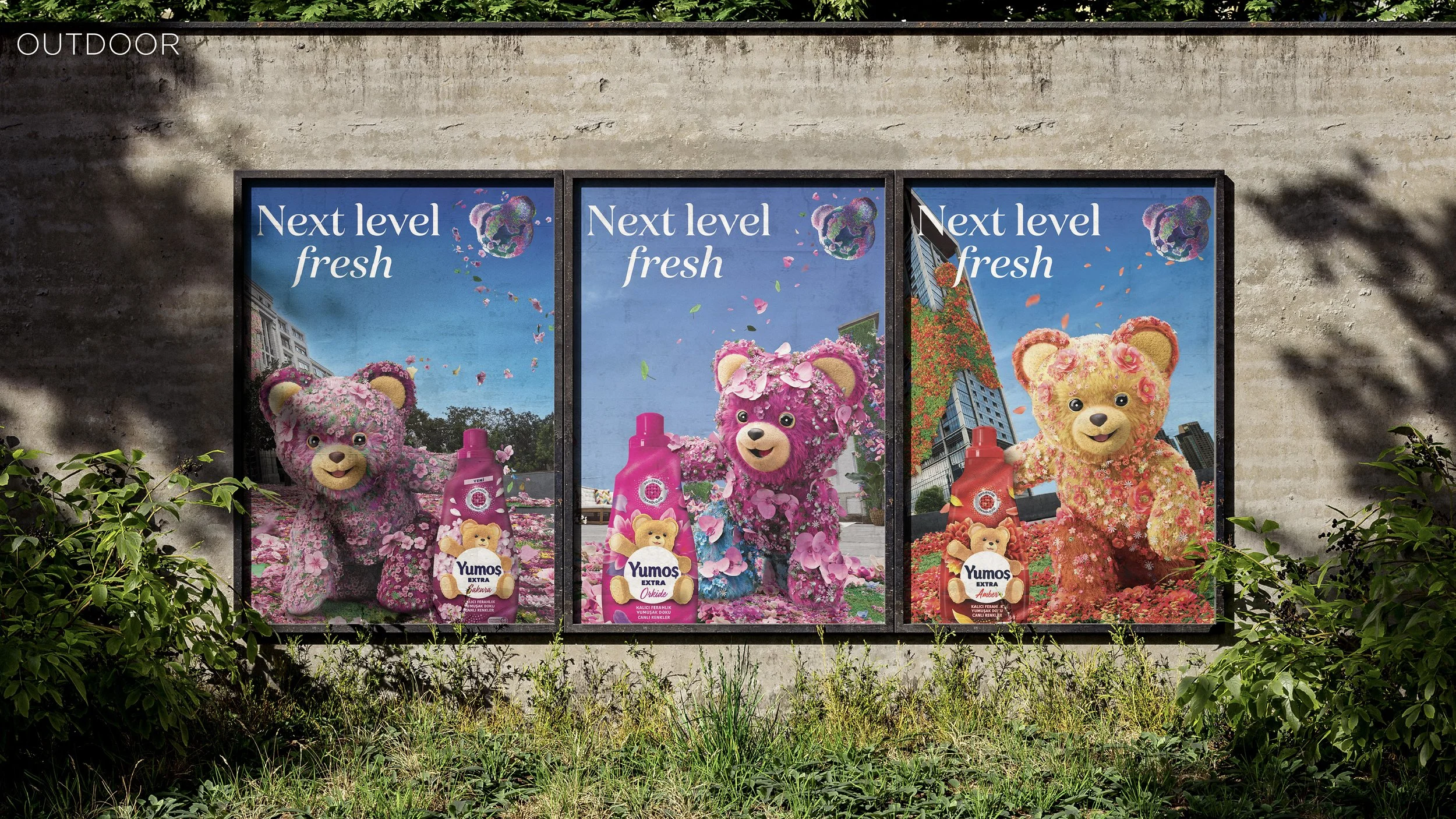 Three outdoor advertising posters on a concrete wall featuring colorful teddy bears made of flowers promoting Yumo's extra fabric softener, with cityscape backgrounds and the slogan 'Next level fresh'.