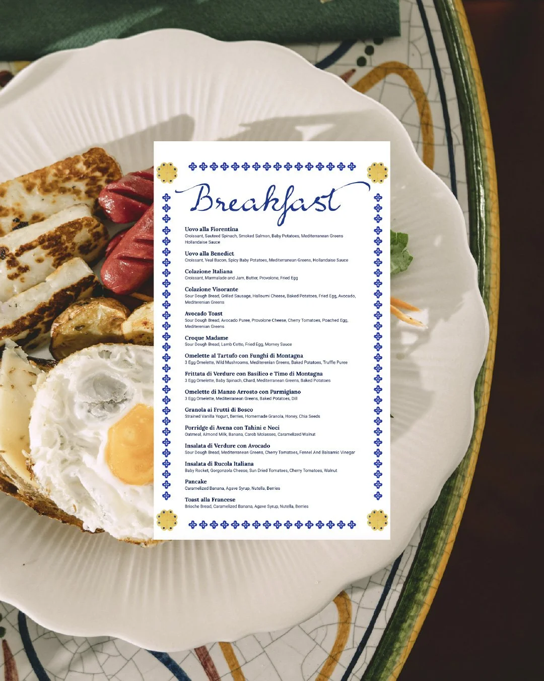A breakfast menu placed on a white plate with various breakfast food items, including eggs, sausages, and toast, on a decorative ceramic plate.