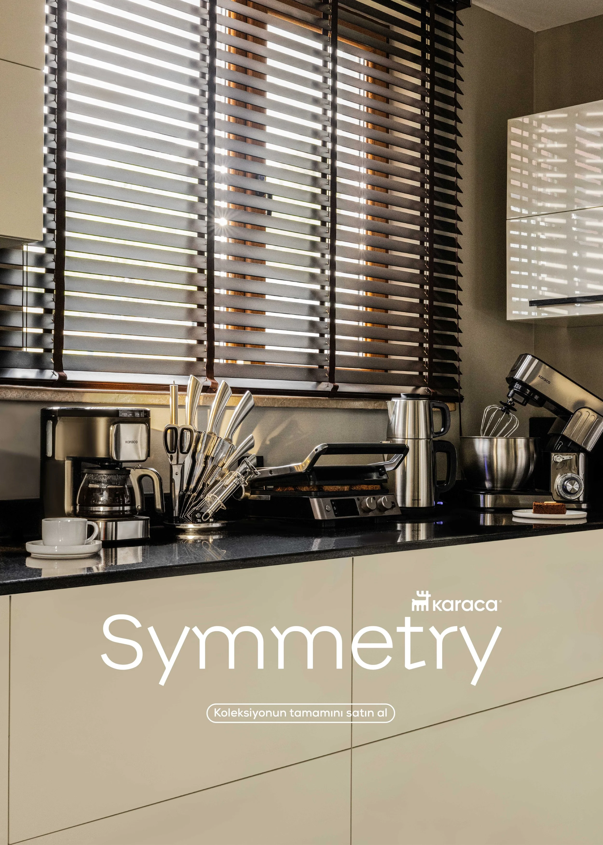 Modern kitchen countertop with coffee maker, knives in a holder, teapot, stand mixer, and plates, with window blinds in the background and promotional text reading 'Symmetry' and 'Koleksiyonun tamamını satın al'.