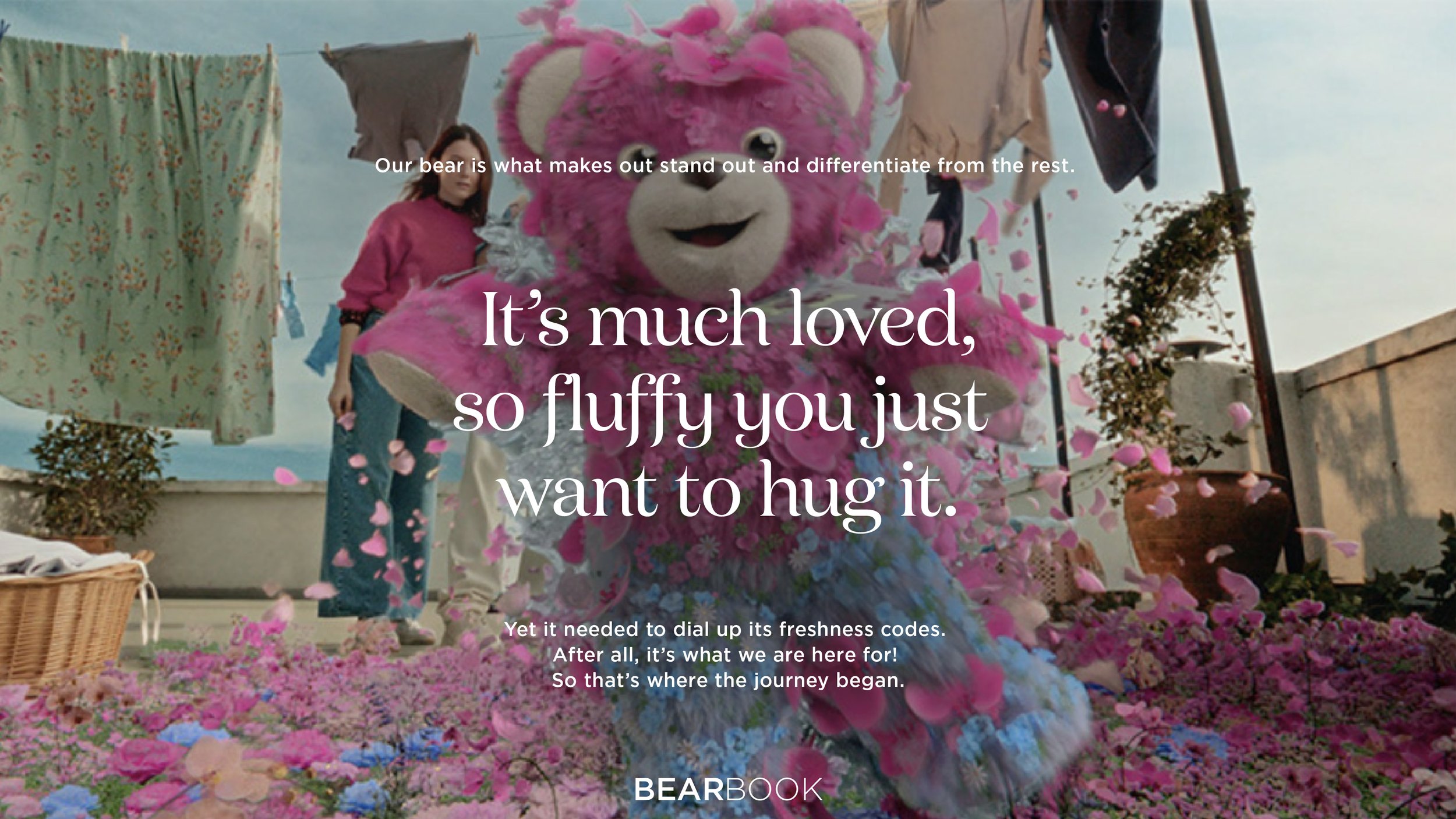 A person in a pink bear costume hugging surrounded by pink and purple flowers on a rooftop with laundry hanging in the background.