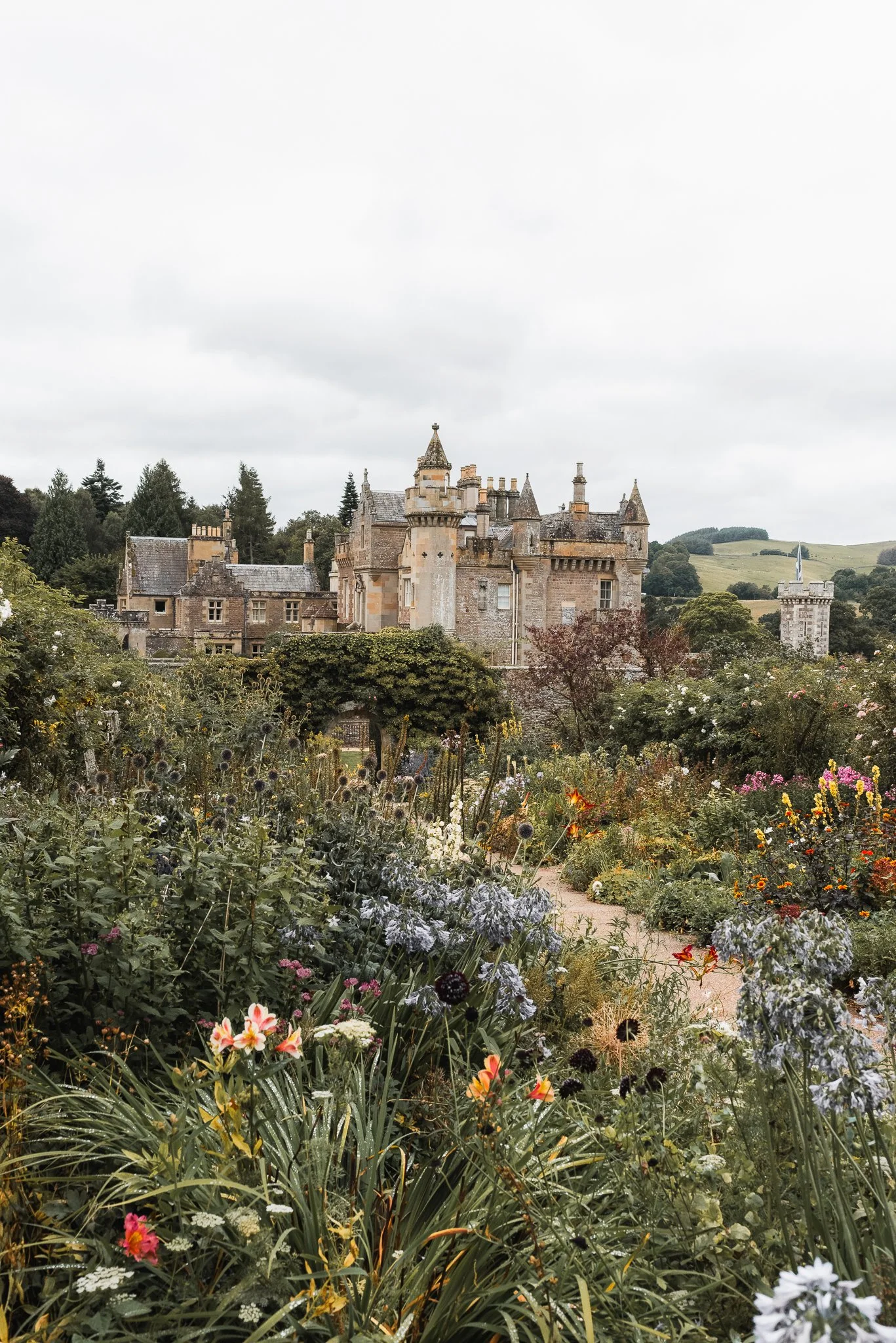 A castle surrounded by a lush garden with colorful flowers and greenery, under a cloudy sky.