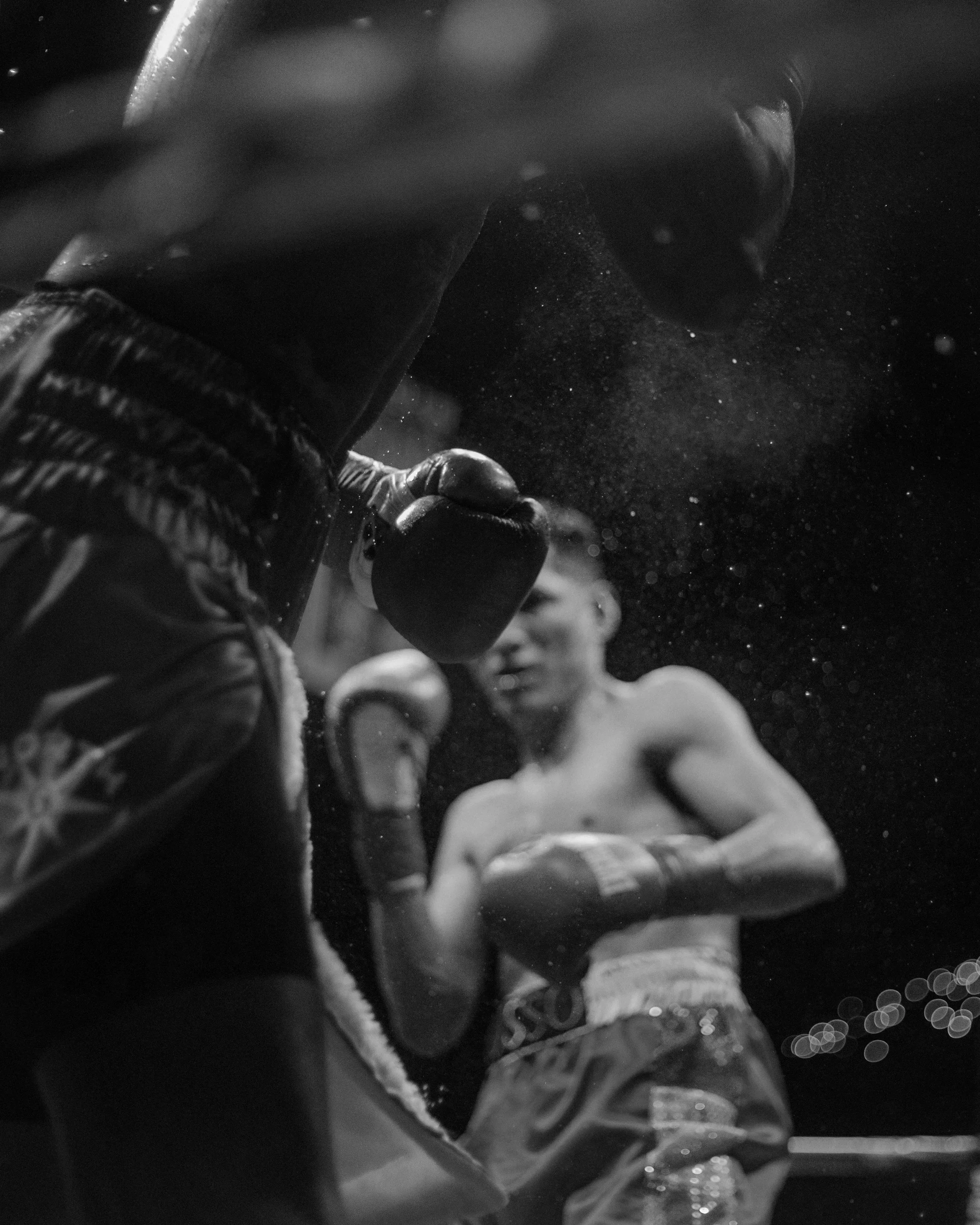 Black and white photograph of two boxers in a ring, one in the foreground throwing a punch, the other in the background with his hands up in a defensive stance.