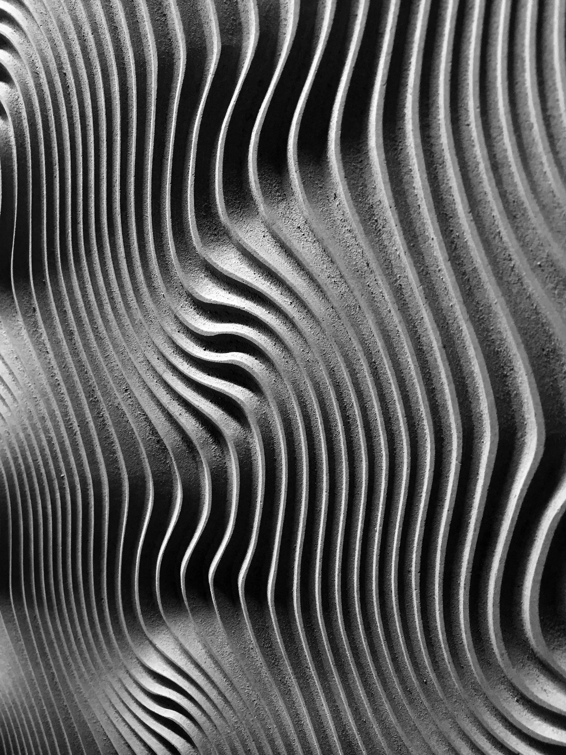 Close-up black and white photo of textured, wavy, metallic surface with parallel ridges and shadows.