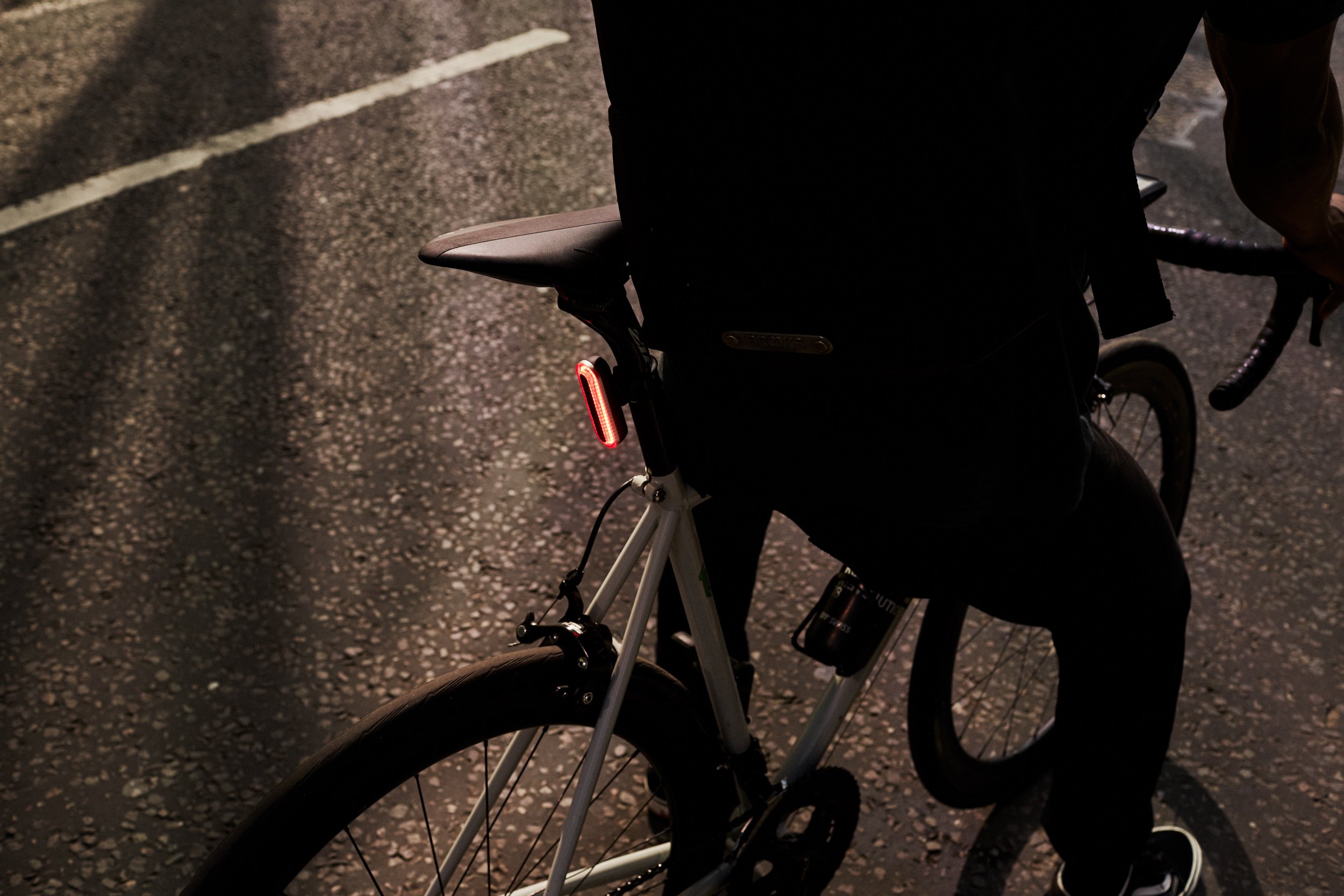 Person riding a bicycle on a dark, dry road at night with a rear LED light on the bike.