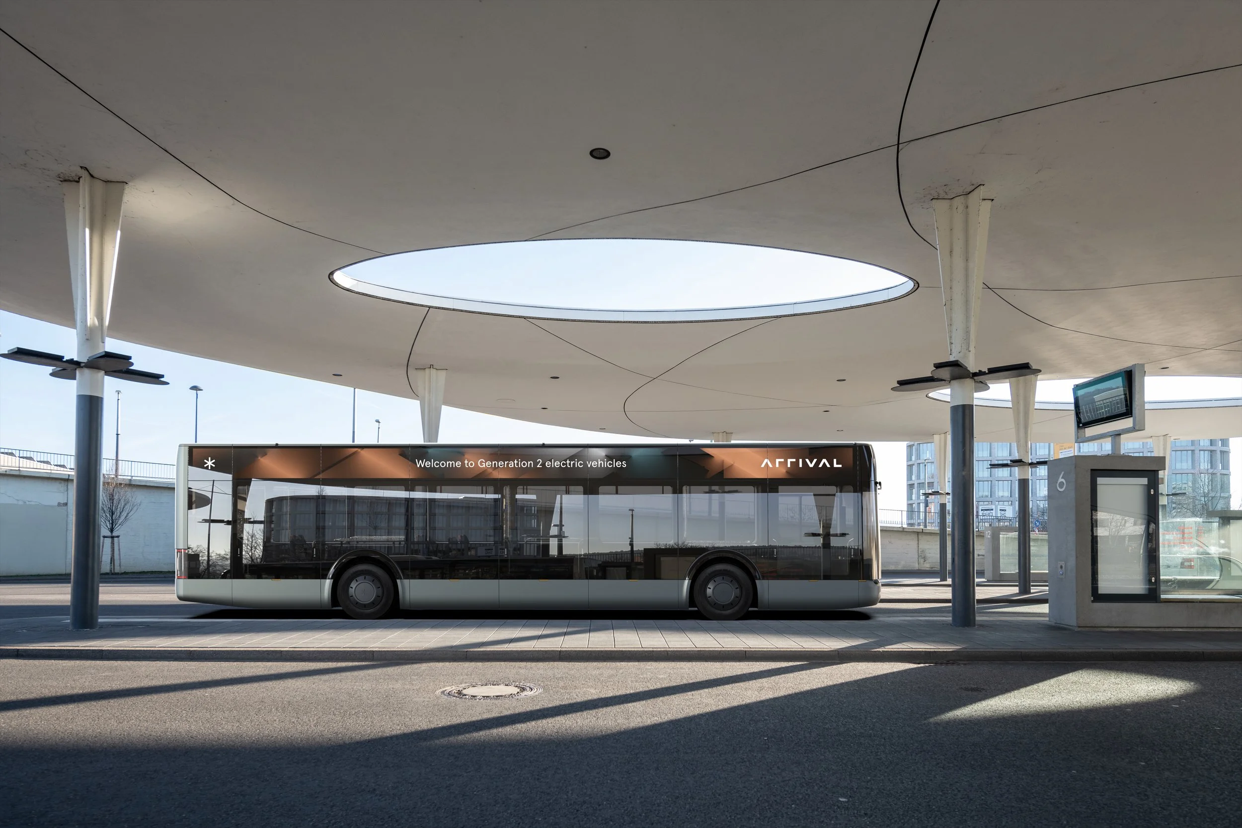 A modern bus terminal with a sleek black electric bus parked at the bus stop under a circular roof structure with large skylight openings.