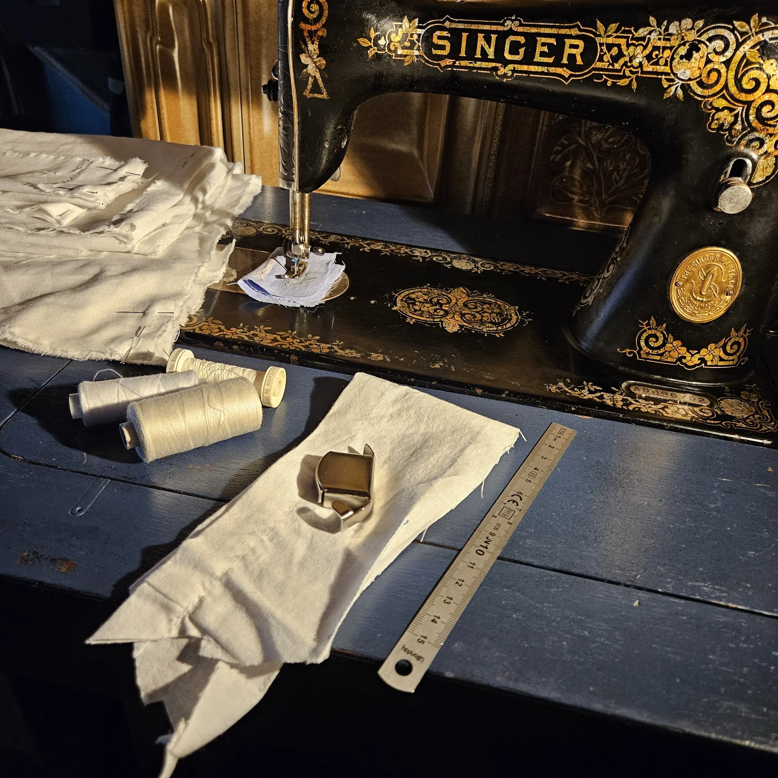 Machine à coudre Singer vintage de 1933 avec du tissu blanc, fils, règle en bois et pièces de couture sur la  table de machine.