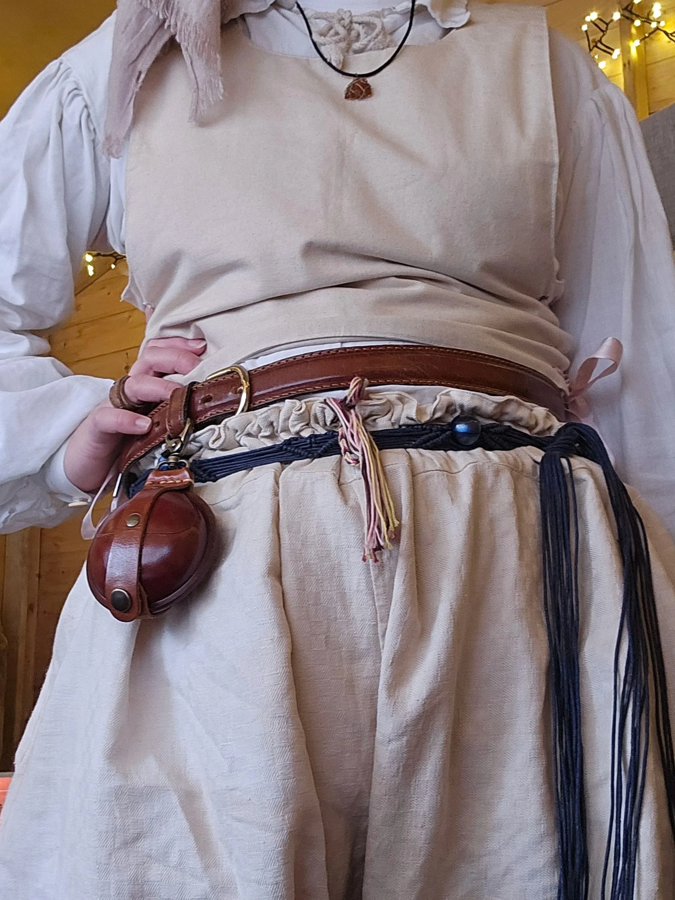 Vêtements inspirés de patrons historique en coton beige et blanc avec accessoires en cuir et cordons, décoration lumineuse en arrière-plan.