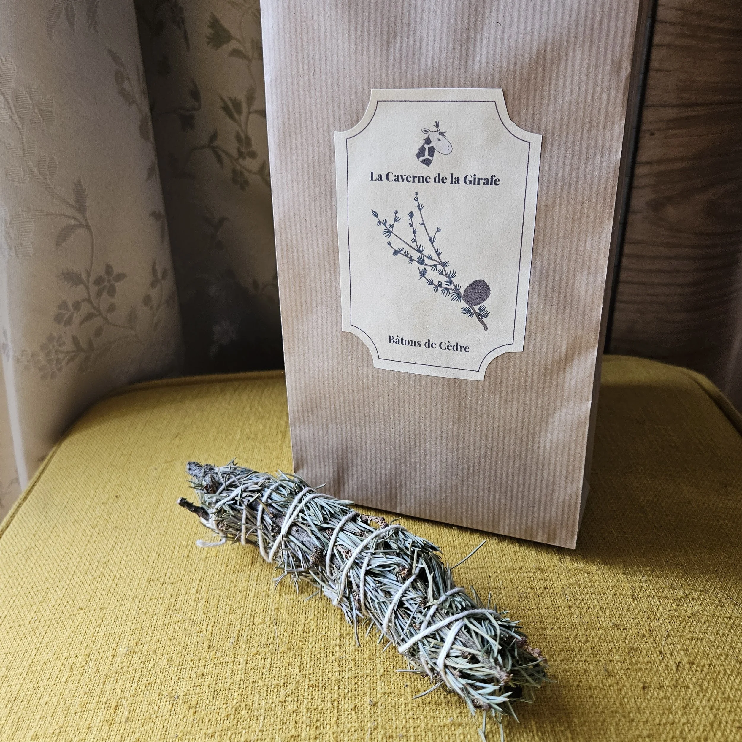 Un bâton de cèdre séché devant une poche en kraft avec une étiquette intitulée "La Caverne de la Girafe".
