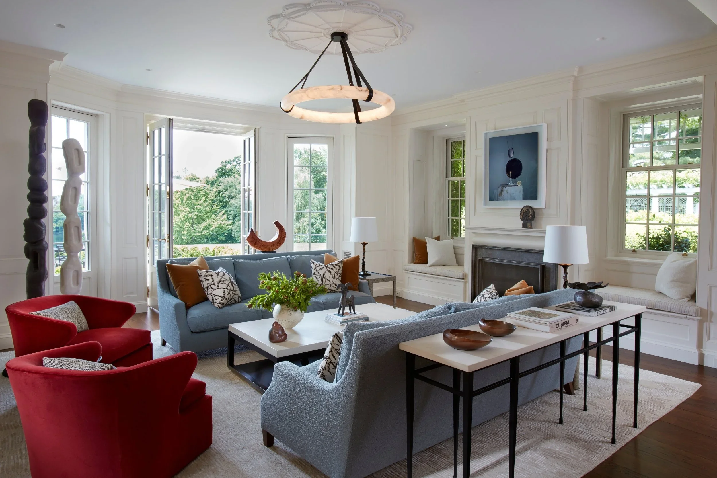 Living room with large windows, white walls, gray and red furniture, decorative items, and a fireplace.