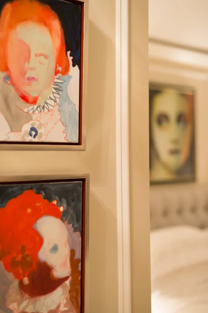 A partial view of three framed portraits hanging on a beige wall with a mirror reflecting two of the portraits in the background.