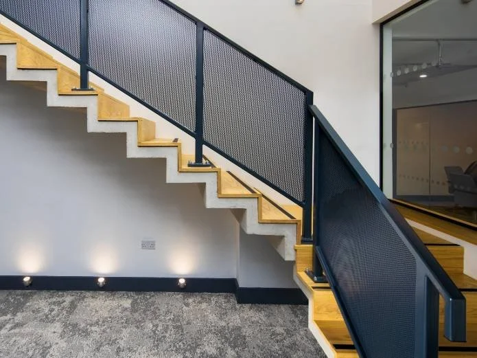 Modern staircase with wooden steps, black metal railing, and perforated metal panels, inside a contemporary building.
