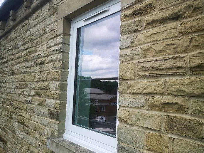 Close-up of a white-framed window on a yellow brick exterior wall, reflecting cloudy sky and neighboring houses.