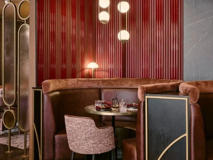 A cozy restaurant corner with a table set for dining, surrounded by plush seating and modern decor, including a red wood-paneled wall and spherical pendant lights.