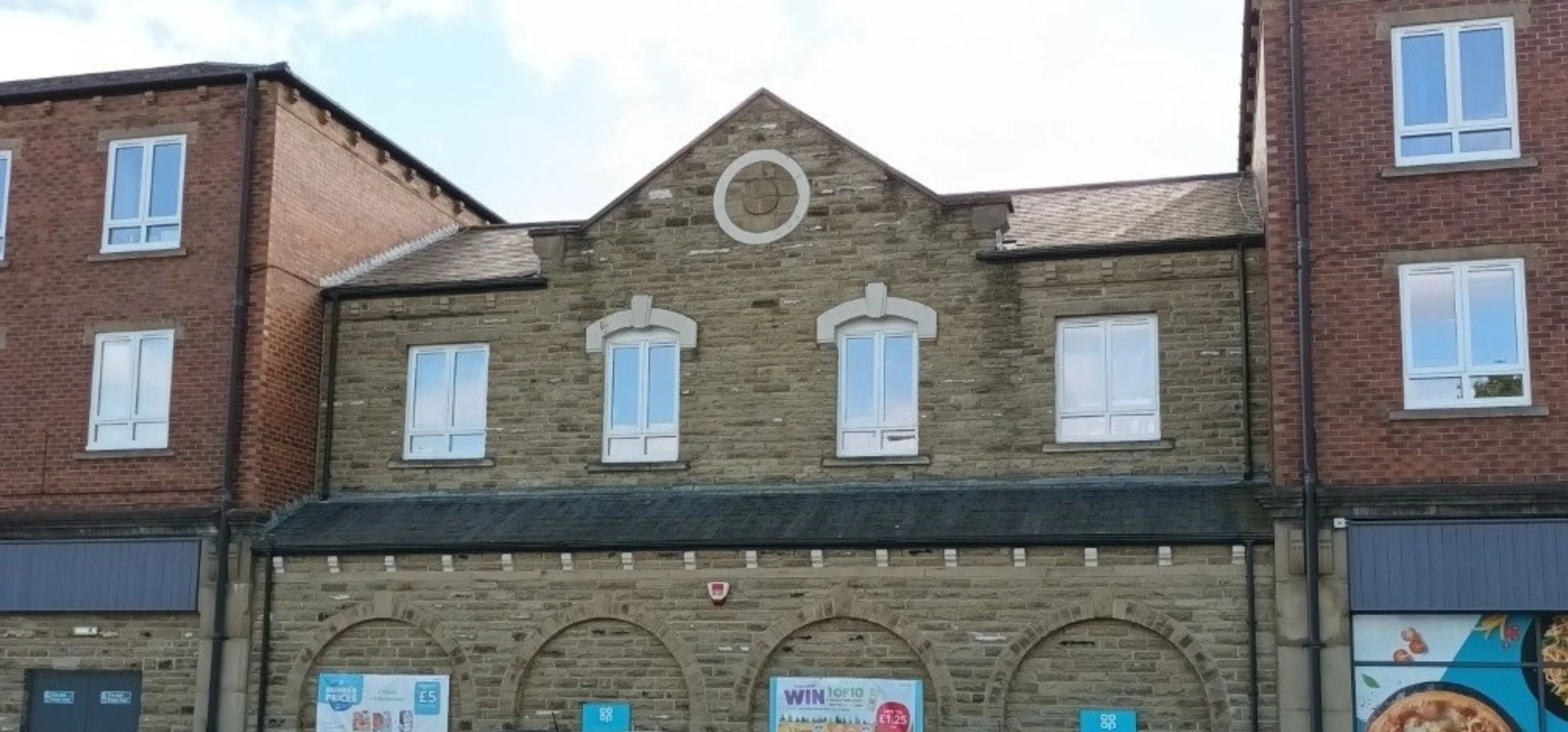 A historic brick and stone building with three symmetrical windows on the upper floor, arches on the lower level, and commercial storefronts at the ground level.