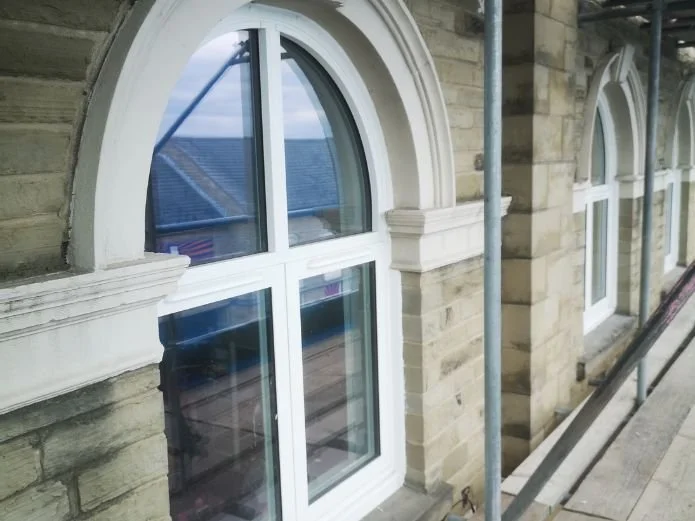 Close-up of a house facade under construction with white-framed arched windows and scaffolding.